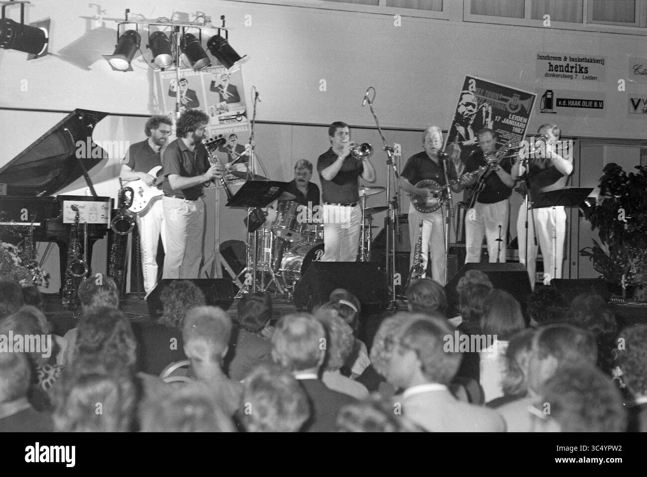 Kenny Ball und sein Jazzman treten während des ersten internationalen Jazz Festivals Noordwijk auf., Noordwijk, 18-08-1990 Whizgle News, Dutch Desk, Niederlande, 1950-2000 Eine lebendige Jazzband tritt auf der Bühne auf und präsentiert verschiedene Instrumente wie Klavier, Schlagzeug und Bläser, während ein engagiertes Publikum die Musik genießt. Plakate und Banner schmücken den Veranstaltungsort und tragen zur lebhaften Atmosphäre der Veranstaltung bei. Stockfoto Kenny Ball und sein Jazzman treten während des ersten internationalen Jazz Festivals Noordwijk auf., Noordwijk, 18-08-1990 Whizgle News, Dutch Desk, Niederlande, 1950-2000 Eine lebendige Jazzband tritt auf der Bühne auf und präsentiert verschiedene Instrumente wie Klavier, Schlagzeug und Bläser, während ein engagiertes Publikum die Musik genießt. Plakate und Banner schmücken den Veranstaltungsort und tragen zur lebhaften Atmosphäre der Veranstaltung bei. Stockfoto