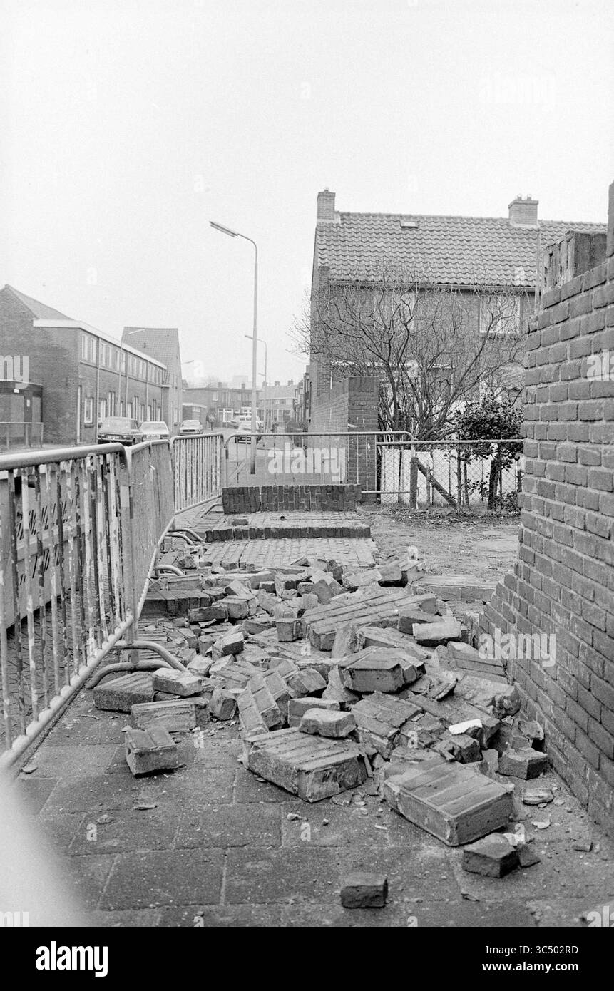 Fallwand, Torricellistraat, IJmuiden, Mauern, IJmuiden, Torricellistraat, Niederlande, 14-04-1986 Whizgle News, Dutch Desk, Niederlande, 1950-2000 Ein Stapel verstreuter Ziegelsteine liegt auf einem leeren Gang, im Hintergrund ist eine teilweise eingestürzte Mauer. Verlassene Gebäude und ein Laternenpfahl sind in der Ferne zu sehen, umgeben von bewachsener Vegetation, was auf Vernachlässigung und Verfall in der Gegend hindeutet. Stockfoto