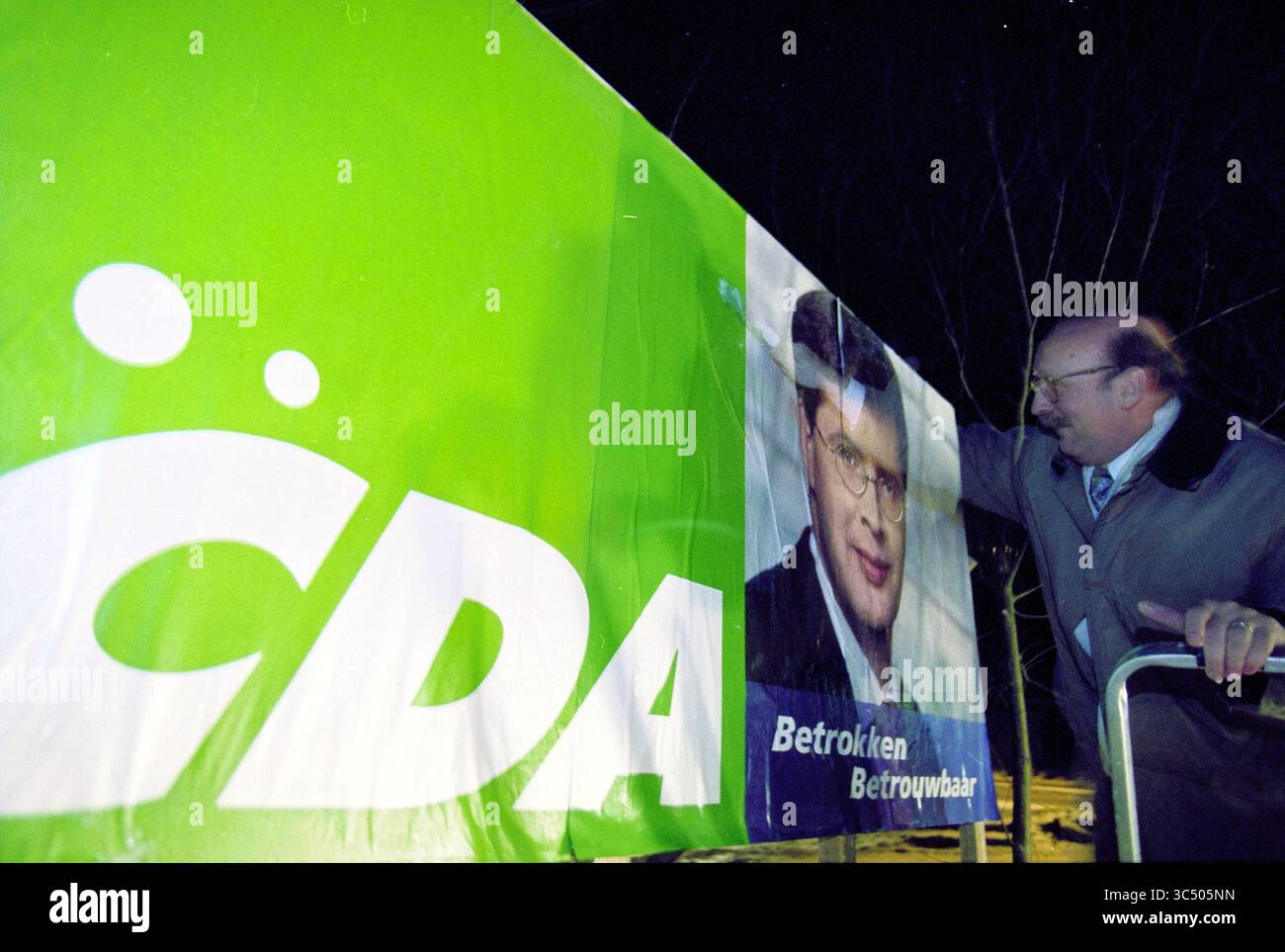 Poster CDA, Zijlweg, Overveen, Overveen, Zijlweg, 10-01-2003 Whizgle News, Dutch Desk, Niederlande, 1950-2000 Ein Mann passt ein großes Kampagnenbanner mit dem CDA-Logo und einem Politikerportrait an und betont die Botschaft von Zuverlässigkeit und Engagement. Stockfoto