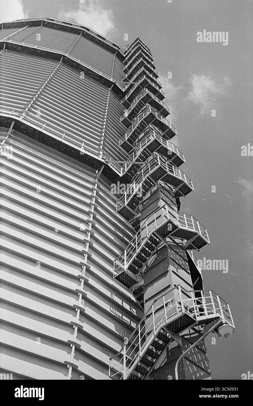 Außerhalb des Silos, 00-06-1972 Whizgle News, Dutch Desk, Niederlande, 1950-2000 Ein hoch aufragendes Industriebauwerk verfügt über eine Reihe von Metalltreppen, die sich vor einem Wolkenkuchen an der Seite nach oben bewegen. Das Design zeigt eine Mischung aus schlanken Linien und geometrischen Mustern, die seine imposante Höhe und seinen funktionalen Zweck betonen. Stockfoto