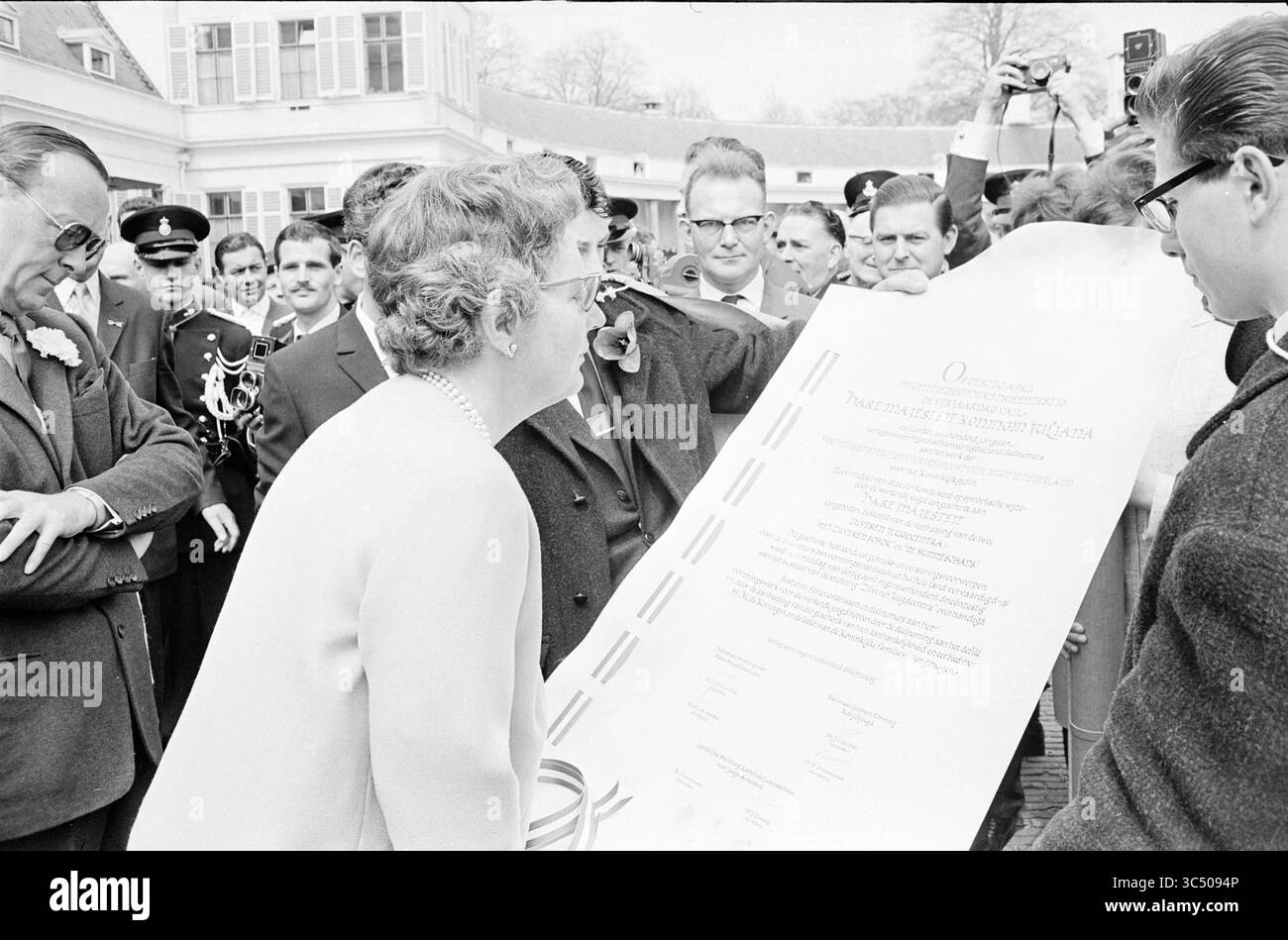 Geburtstag und Porträts Ihrer Majestät, königliche Empfänge und königliche Besuche, königliche Geburtstage, 30 04.04.1963 Whizgle News, Dutch Desk, Niederlande, 1950-2000 Eine freudige Menschenmenge versammelt sich, um die Enthüllung eines wichtigen Dokuments zu feiern, wobei eine begeisterte Frau die Anklage anführt, während sie die große, präsentierte Schriftrolle untersucht. Gesichter drücken Begeisterung und Neugier aus und betonen die Wichtigkeit des Anlasses. Stockfoto