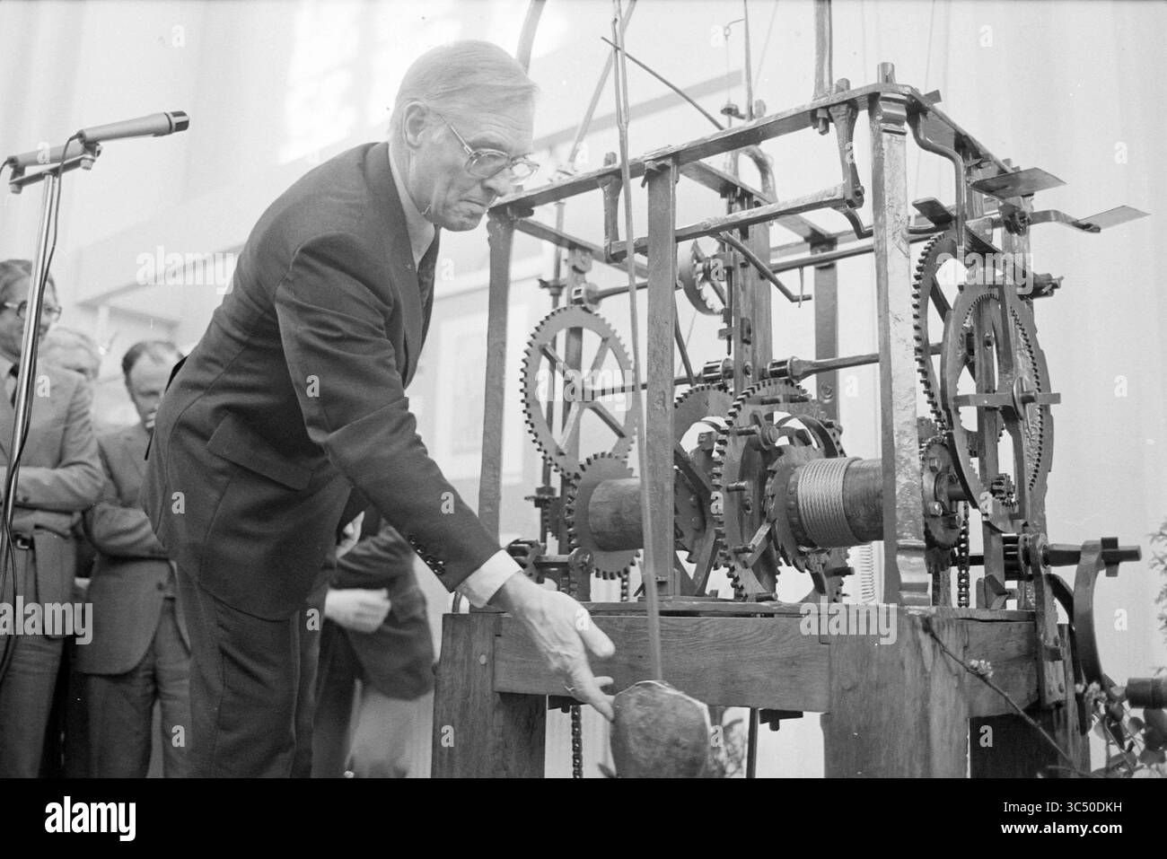 Eröffnung der Ausstellung "das Archiv: Haarlem Gedächtnis", anlässlich 125 Jahre Stadtarchiv, durch Bürgermeister Reehorst, in der Janskerk., Jahrestag, Jahrestag, Haarlem, Jansstraat 40, Niederlande, 25-03-1982 Whizgle News, Dutch Desk, Niederlande, 1950-2000 Ein Mann interagiert mit einem komplexen mechanischen Gerät mit verschiedenen Gängen und Hebeln und demonstriert seine Funktionsweise einem aufmerksamen Publikum im Hintergrund. Stockfoto
