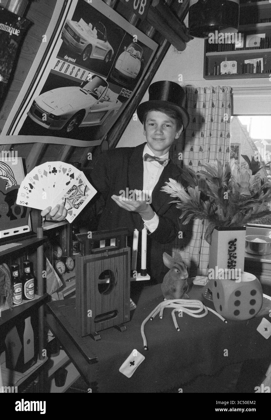 Bart van Capelle, Zauberer, 14 Jahre alt, Magic, 24-10-1989 Whizgle News, Dutch Desk, Niederlande, 1950-2000 Ein junger Magier in formeller Kleidung präsentiert ein Kartenspiel, das seine Fähigkeiten mit einem charmanten Lächeln unter Beweis stellt. Um ihn herum sind verschiedene magische Requisiten, ein flauschiges Kaninchen und dekorative Elemente, die eine skurrile Atmosphäre hervorrufen. Stockfoto