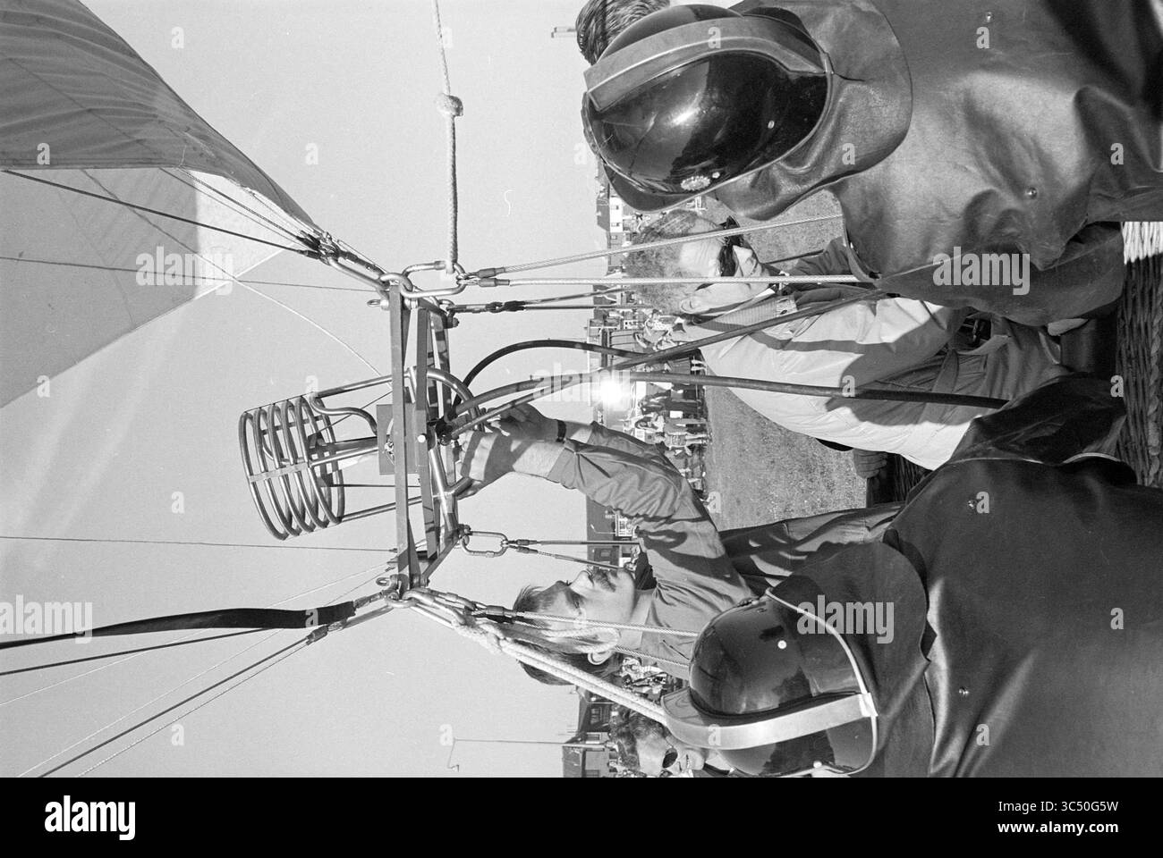 Heißluftballon aufblasen, 00-05-1977 Whizgle News, Dutch Desk, Niederlande, 1950-2000 Eine Gruppe von Einzelpersonen bereitet einen Heißluftballon für den Flug vor, wobei eine Person das Brennersystem anpasst, während andere genau beobachten, alle in Schutzkleidung gekleidet. Stockfoto