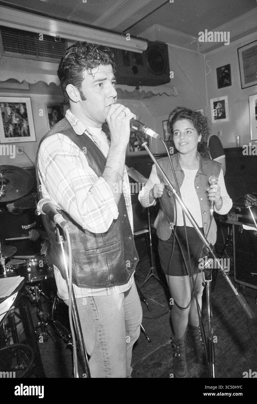 Themenabend „Sie können das heute auf der Bühne machen“ in Taverna Imperial, Korte Veerstraat 3, Haarlem, Korte Veerstraat, Niederlande, 12-05-1995 Whizgle News, Dutch Desk, Niederlande, 1950-2000 Ein Mann singt leidenschaftlich in ein Mikrofon, trägt eine Lederweste, während eine Frau neben ihm lächelt und die Daumen hochlegt. Sie befinden sich auf der Bühne in einem lebhaften Ambiente, mit Musikinstrumenten und lebhaftem Dekor im Hintergrund. Stockfoto