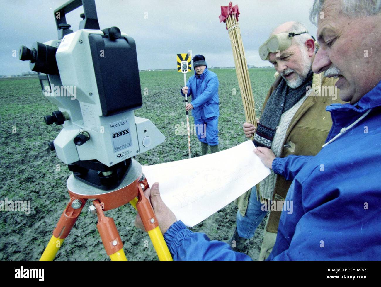 R. van Vliet, Keukenhof, Rijsenhout, Rijsenhout, 21.03.1999 Whizgle News, Dutch Desk, Niederlande, 1950-2000 zwei Personen untersuchen ein großes Stück Papier, während sie ein Vermessungsinstrument auf einem Feld bedienen. Eine trägt eine Schutzbrille und eine andere steht in der Nähe mit Messstäben, die anzeigen, dass sie an Landvermessungen oder Kartierungen beteiligt sind. Die Umwelt erscheint offen und landwirtschaftlich, was auf Arbeiten im Zusammenhang mit dem Bau oder der Bodenentwicklung hindeutet. Stockfoto