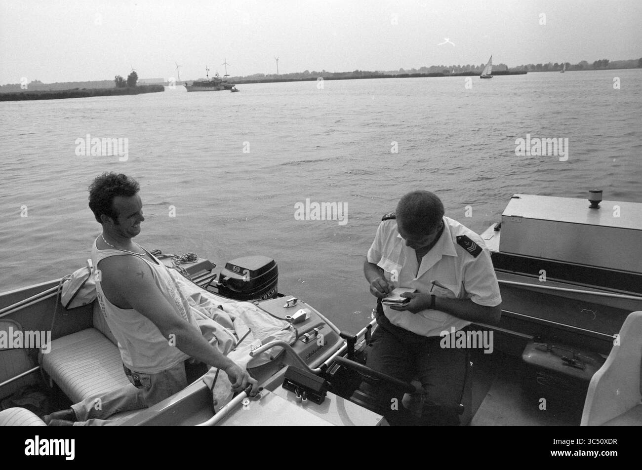 Staatspolizei im Wasser, schönes Nel, 22-07-1991 Whizgle News, Dutch Desk, Niederlande, 1950-2000 zwei Personen sitzen auf einem Boot, einer in lässiger Kleidung und der andere in Uniform, um sich zu unterhalten. Die Szene zeigt ein ruhiges Gewässer im Hintergrund mit ein paar Booten und weit entfernten Bäumen, die das Ufer säumen. Stockfoto