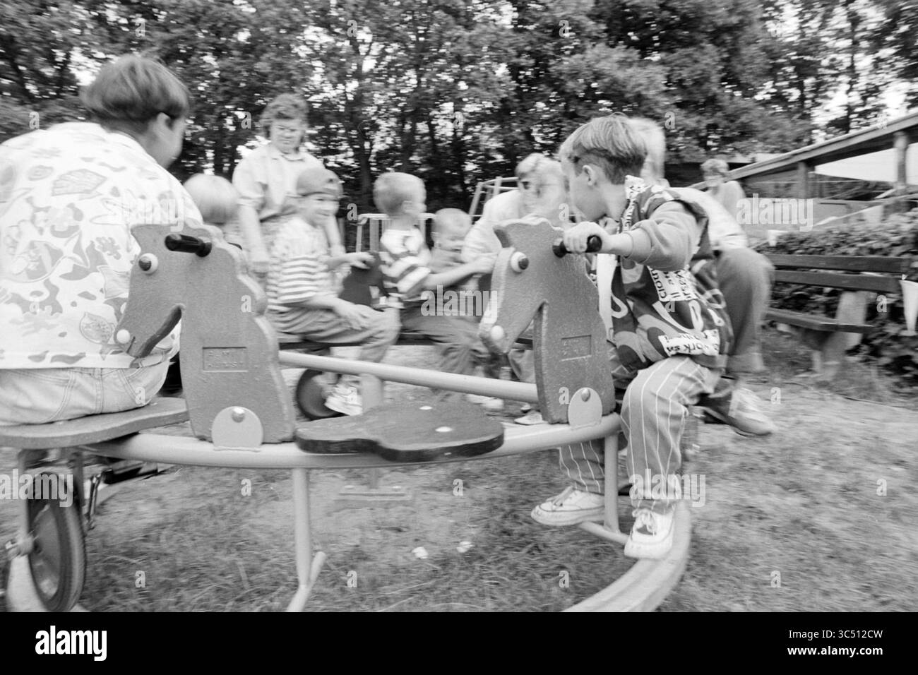 Offizielle Eröffnung des Santpoort Spielzentrums, Santpoort, 28-08-1992 Whizgle News, Dutch Desk, Niederlande, 1950-2000 Eine lebhafte Szene, in der Kinder fröhlich auf einem Karussell spielen, umgeben von Grün und Erwachsenen in einer lebhaften Spielplatzatmosphäre mit ihnen interagieren. Lachen und Energie erfüllen die Luft, während sich die Kinder abwechselnd drehen und den Moment gemeinsam genießen. Stockfoto