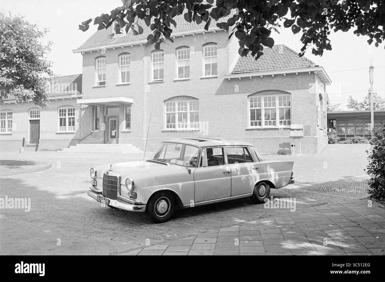 Taxistand Bloemendaal, Taxi, 2-07-1969 Whizgle News, Dutch Desk, Niederlande, 1950-2000 Eine klassische Limousine parkt vor einem charmanten Backsteinschulgebäude, mit großen Fenstern und einem einladenden Eingang, umgeben von Grün. Stockfoto