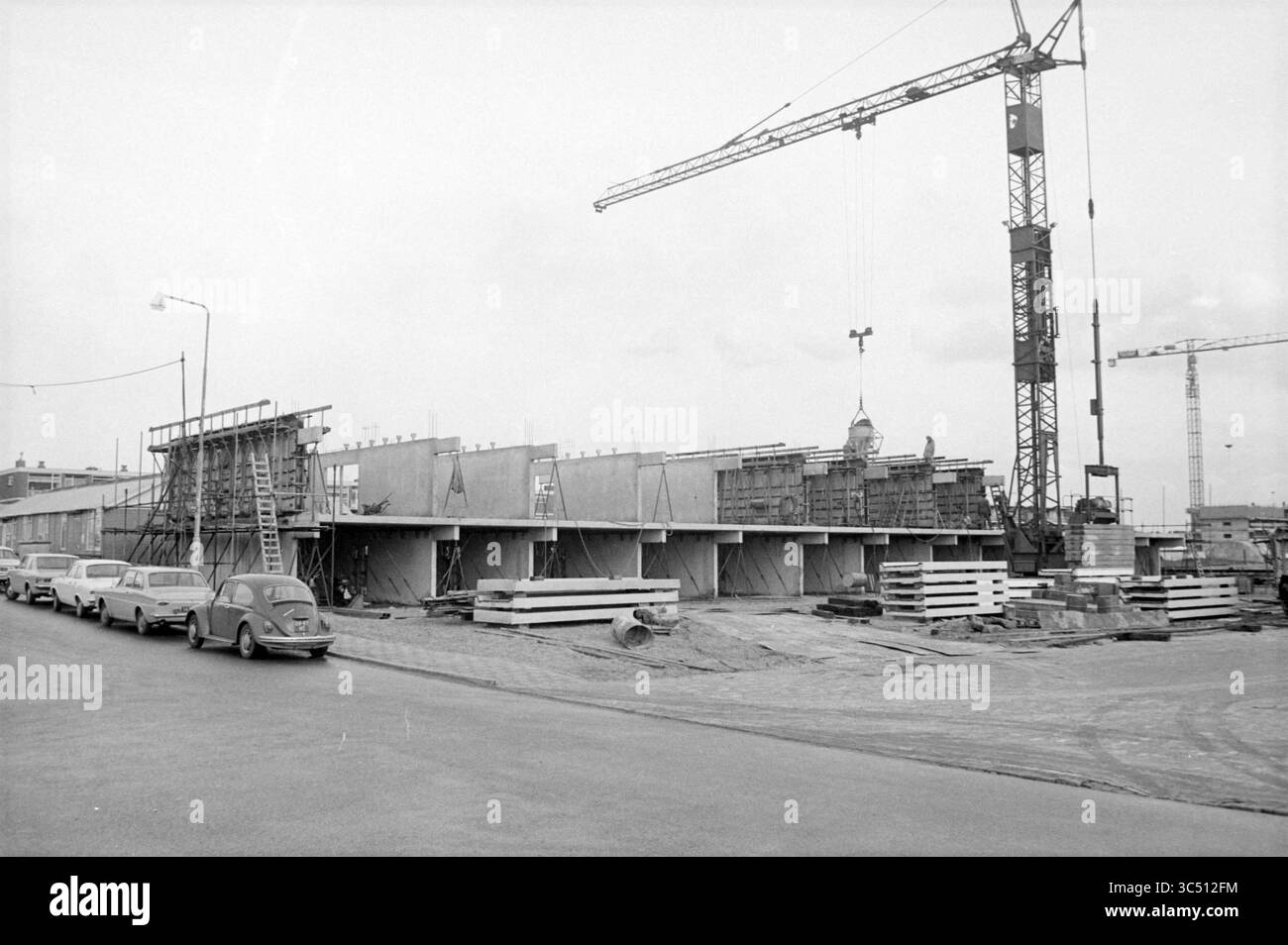 Häuser im Bau, 29-11-1971 Whizgle News, Dutch Desk, Niederlande, 1950-2000 Eine Baustelle zeigt den Bau von Bauwerken mit Gerüsten und Kränen, während geparkte Autos die Straße säumen. Stockfoto