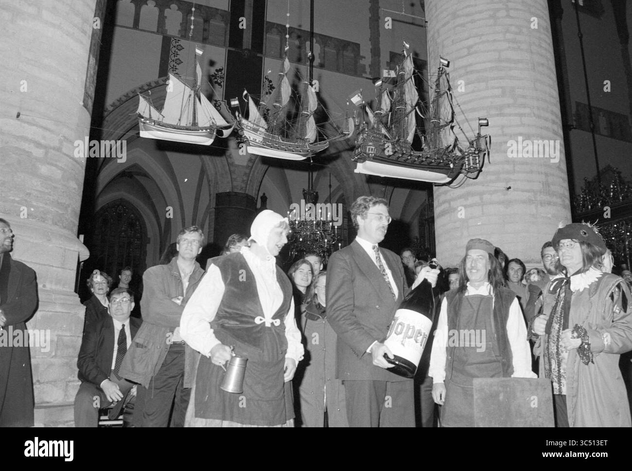 Haarlem Jopen Beer, Haarlem, Niederlande, 10-11-1994 Whizgle News, Dutch Desk, Niederlande, 1950-2000 Ein festliches Treffen zeigt einen Mann in einem Anzug, der eine große Flasche mit der Aufschrift „Cider“ hält, umgeben von kostümierten Personen, darunter eine Frau in historischer Kleidung. Über ihnen hängen Modellschiffe von der Decke und verleihen der Szene einen skurrilen Touch. Das Publikum wirkt engagiert und fröhlich und trägt zur feierlichen Atmosphäre bei. Stockfoto