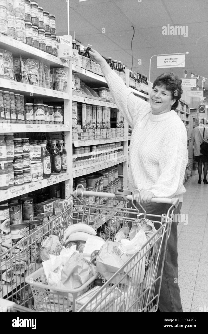 Vomar Heerhugowaard, Heerhugowaard, 09-04-1992 Whizgle News, Dutch Desk, Niederlande, 1950-2000 Eine fröhliche Käuferin greift in einem Supermarkt nach einem Produkt, während ihr Wagen mit verschiedenen Artikeln gefüllt ist, darunter Bananen und verpackte Waren. Die hellen Gänge bieten eine gut sortierte Auswahl an Lebensmitteln. Stockfoto