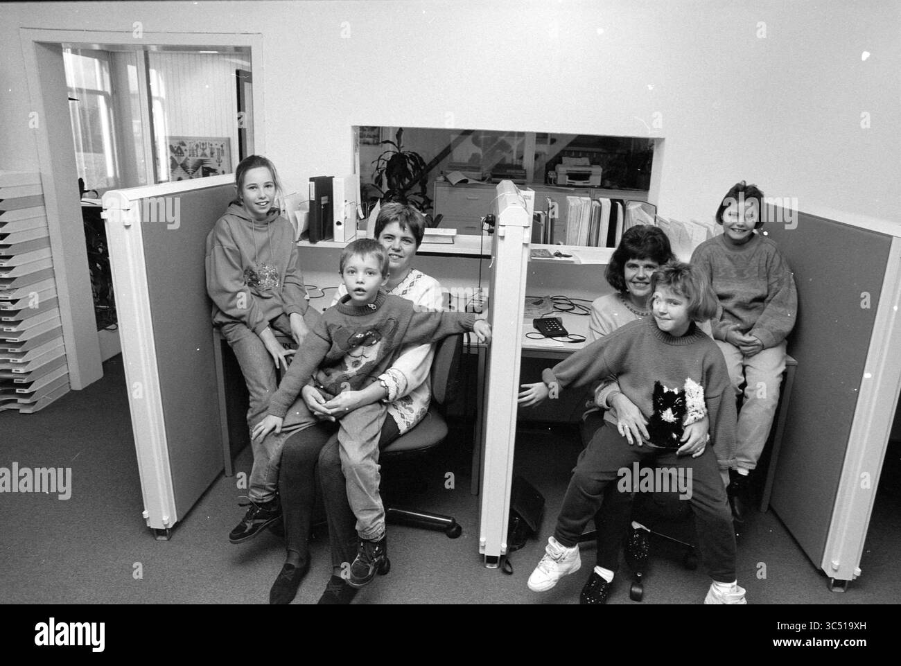 TelePoint, in Verbindung mit Kinderbetreuung Haarlem, Haarlem, Niederlande, 02-11-1992 Whizgle News, Dutch Desk, Niederlande, 1950-2000 Eine Gruppe von sechs Personen, darunter Kinder und Erwachsene, versammelt sich in einem Büro, das an Arbeitsplätzen sitzt, die durch Trennwände getrennt sind. Die Erwachsenen scheinen sich zu unterhalten, während die Kinder spielerisch miteinander interagieren und ein kleines Haustier halten, was eine fröhliche und entspannte Atmosphäre schafft. Stockfoto