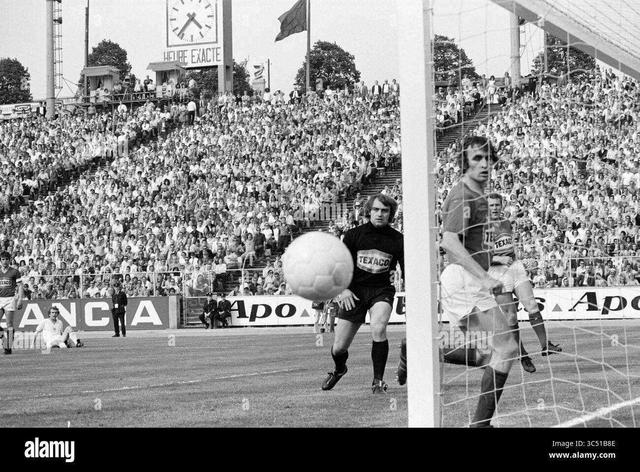 Football Standard - Anderlecht, Football, 27-05-1973 Whizgle News, Dutch Desk, Niederlande, 1950-2000 Ein Torhüter sieht zu, wie ein Fußballball ins Netz zusteuert, während Spieler und eine überfüllte Menge eifrig auf das Ergebnis des Augenblicks warten. Flaggen flattern im Hintergrund, was die Spannung des Spiels erhöht. Stockfoto