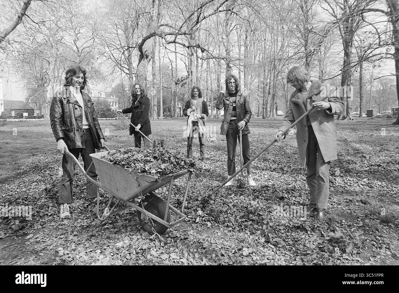 Group Jumbo, Musik, 26-04-1971 Whizgle News, Dutch Desk, Niederlande, 1950-2000 Eine Gruppe von fünf Einzelpersonen, die in legeren Kleidern gekleidet sind, beschäftigt sich mit Gartenarbeiten, Harken und Blätter sammeln. Eine Person drückt eine Schubkarre voller Laub, während andere bei der Aufgabe helfen, umgeben von hohen Bäumen und einer weitläufigen parkähnlichen Umgebung. Stockfoto