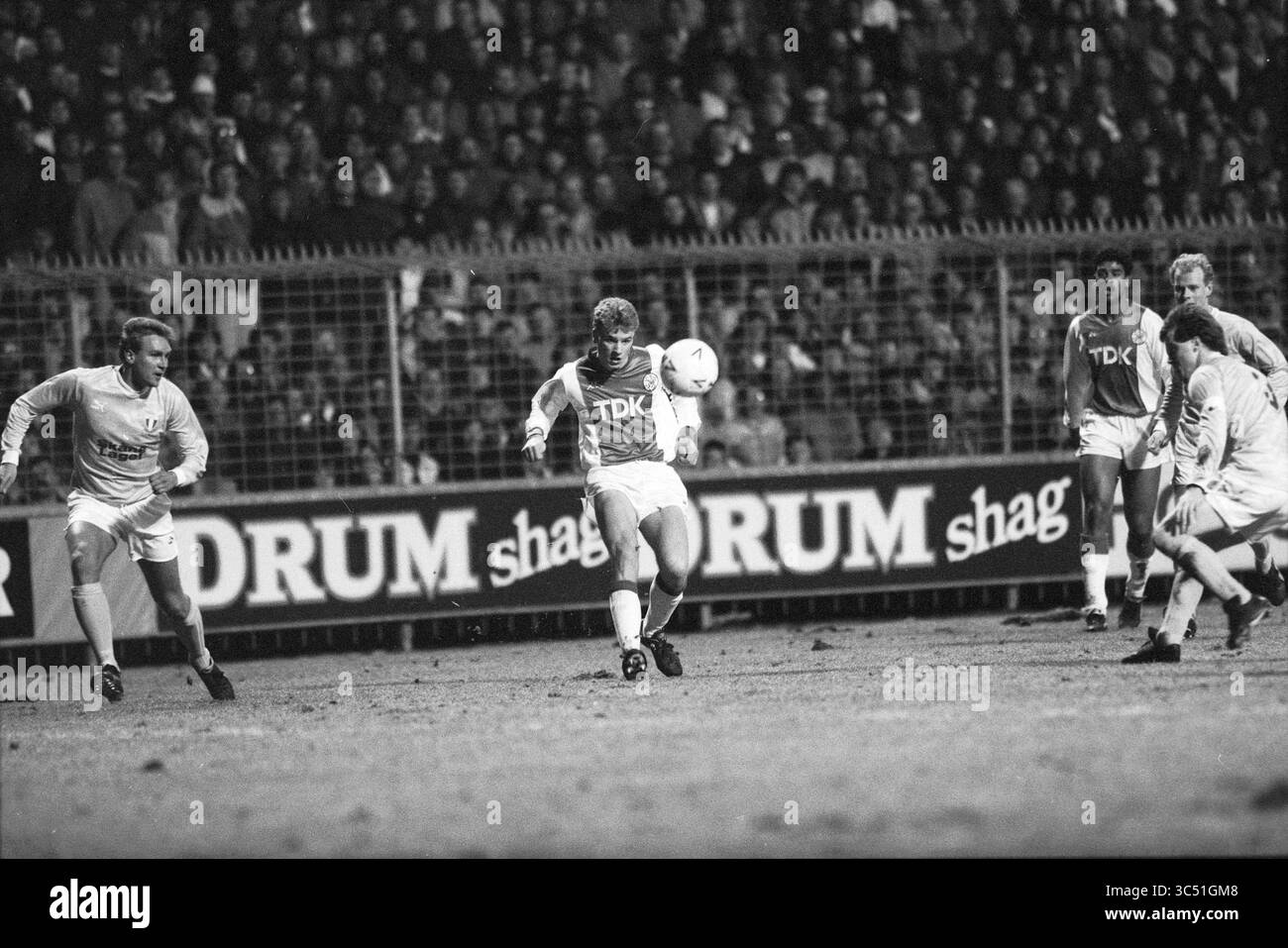 Ajax Football Match Whizgle News, Dutch Desk, Niederlande, 1950-2000 Ein angespannter Moment auf dem Fußballfeld, in dem ein Spieler den Ball gekonnt steuert, während Teamkollegen und Gegner den nächsten Zug erwarten, umgeben von einer Menge enthusiastischer Zuschauer. Stockfoto