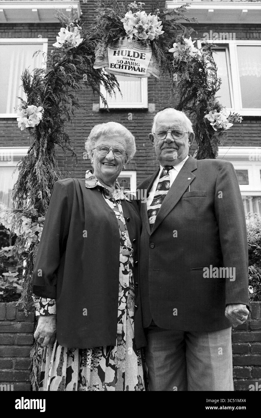 Verheiratet seit 50 Jahren, Familie v.d. Bag, 26-05-1997 Whizgle News, Dutch Desk, Niederlande, 1950-2000 Ein fröhliches älteres Ehepaar steht stolz vor einem geschmückten Torbogen zusammen und feiert mit Blumenschmuck und einem Schild, das ihre langjährige vereinigung ehrt, einen besonderen Meilenstein. Beide tragen formelle Kleidung, die Wärme und Glück bei diesem wichtigen Anlass ausstrahlt. Stockfoto