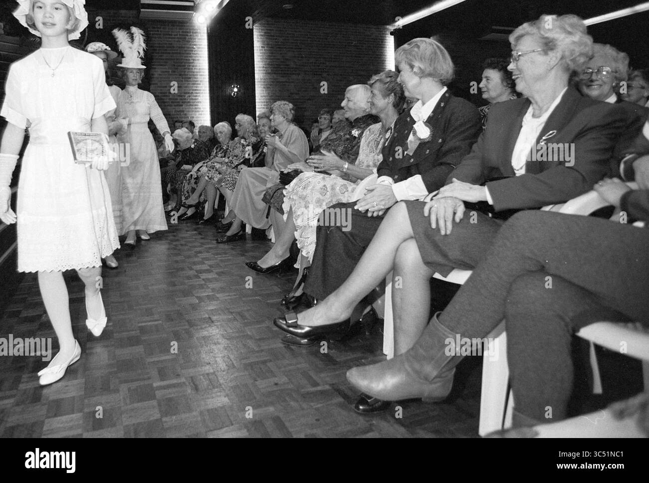 Modenschau für Ned Housewives Association, 22-10-1991 Whizgle News, Dutch Desk, Niederlande, 1950-2000 Eine Gruppe elegant gekleideter Frauen sitzt aufmerksam in einem Saal und sieht sich eine Modenschau an. Im Vordergrund geht ein Model in einem Vintage-Outfit anmutig vorbei und zeigt die Kleidung. Das Publikum ist voller Lächeln und Neugierde und besteht aus Frauen unterschiedlichen Alters, die jeweils in stilvoller Kleidung gekleidet sind. Die Atmosphäre ist lebendig und engagiert, was ein Gefühl der Feier und Wertschätzung für Mode widerspiegelt. Stockfoto