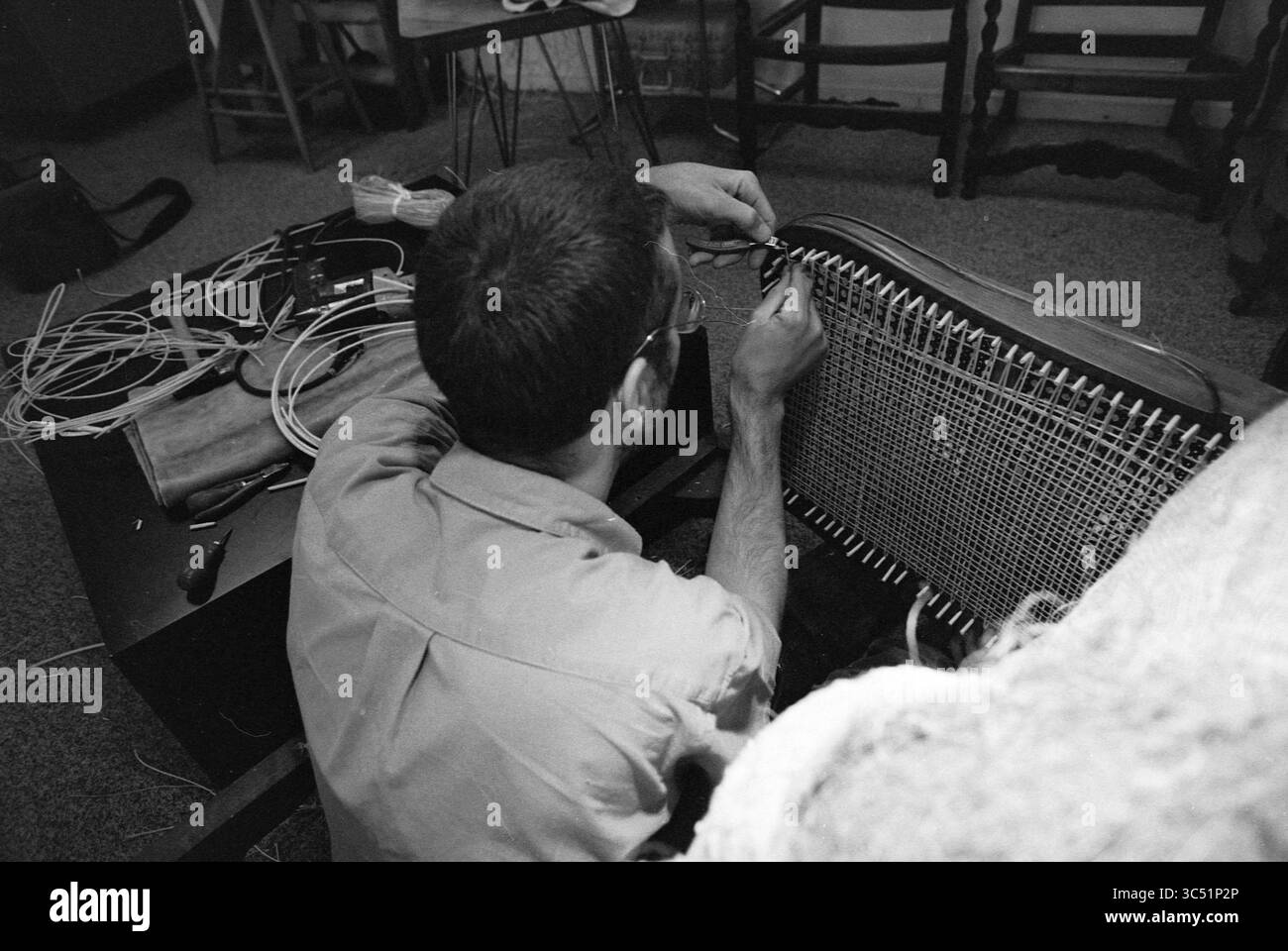 Alte Berufe wie Gestell-, Stuhl- und Korbmacher, 01-06-1990 Whizgle News, Dutch Desk, Niederlande, 1950-2000 Eine Person sitzt und konzentriert sich darauf, ein Möbelstück zu reparieren, aufwändig Fäden in einen Sitz zu weben. Um sie herum befinden sich verschiedene Werkzeuge und Materialien, die im Herstellungsprozess verwendet werden. Stockfoto