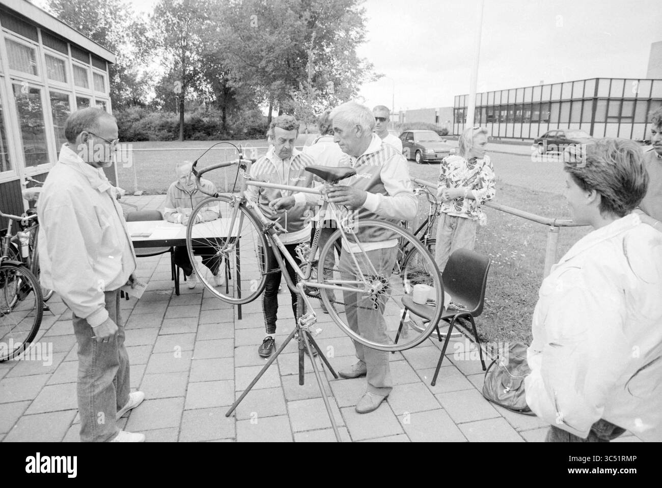 Fahrradinspektionsmücke rund Clubhaus excelsior, Muggeronde, 02-08-1989 Whizgle News, Dutch Desk, Niederlande, 1950-2000 Eine Gruppe von Personen, die sich als Lehrer versammelt haben, demonstriert Techniken zur Wartung von Fahrrädern, hebt ein Fahrrad auf einem Reparaturstand an, während andere aufmerksam beobachten. Die Umgebung scheint eine Outdoor-Werkstatt oder eine Community-Veranstaltung zu sein. Stockfoto
