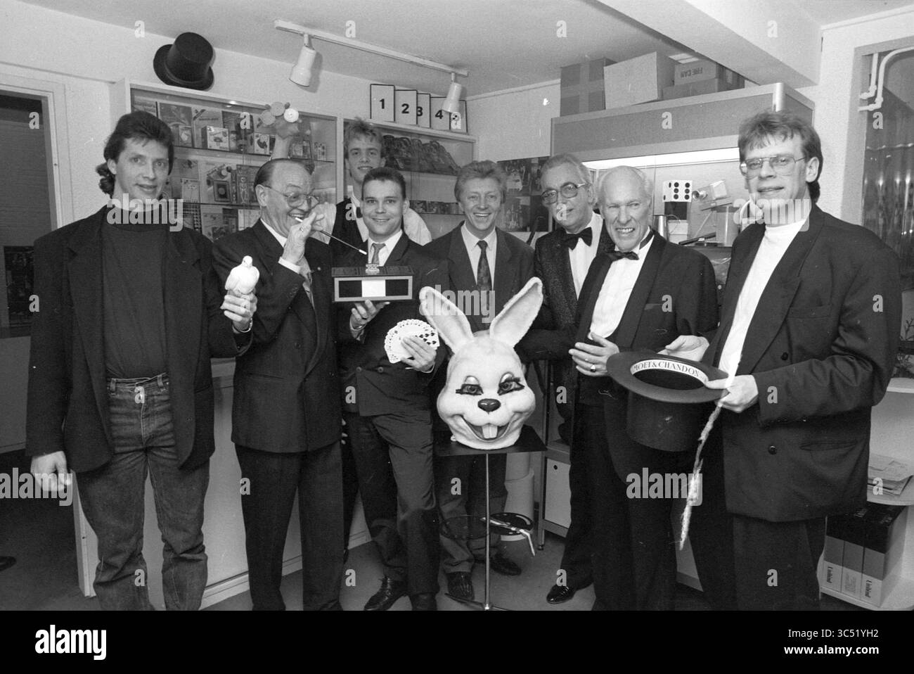 Haarlem Magicians von Richard Ross, Haarlem, Niederlande, 03-03-1991 Whizgle News, Dutch Desk, Niederlande, 1950-2000 Eine Gruppe von acht Männern, die in formeller Kleidung gekleidet sind, steht zusammen in einem Raum, der mit verschiedenen Zauberrequisiten gefüllt ist. Sie lächeln und posieren verspielt mit einem großen Hasen-Kopfstück und anderen magischen Gegenständen, die eine festliche Atmosphäre vermitteln. Stockfoto