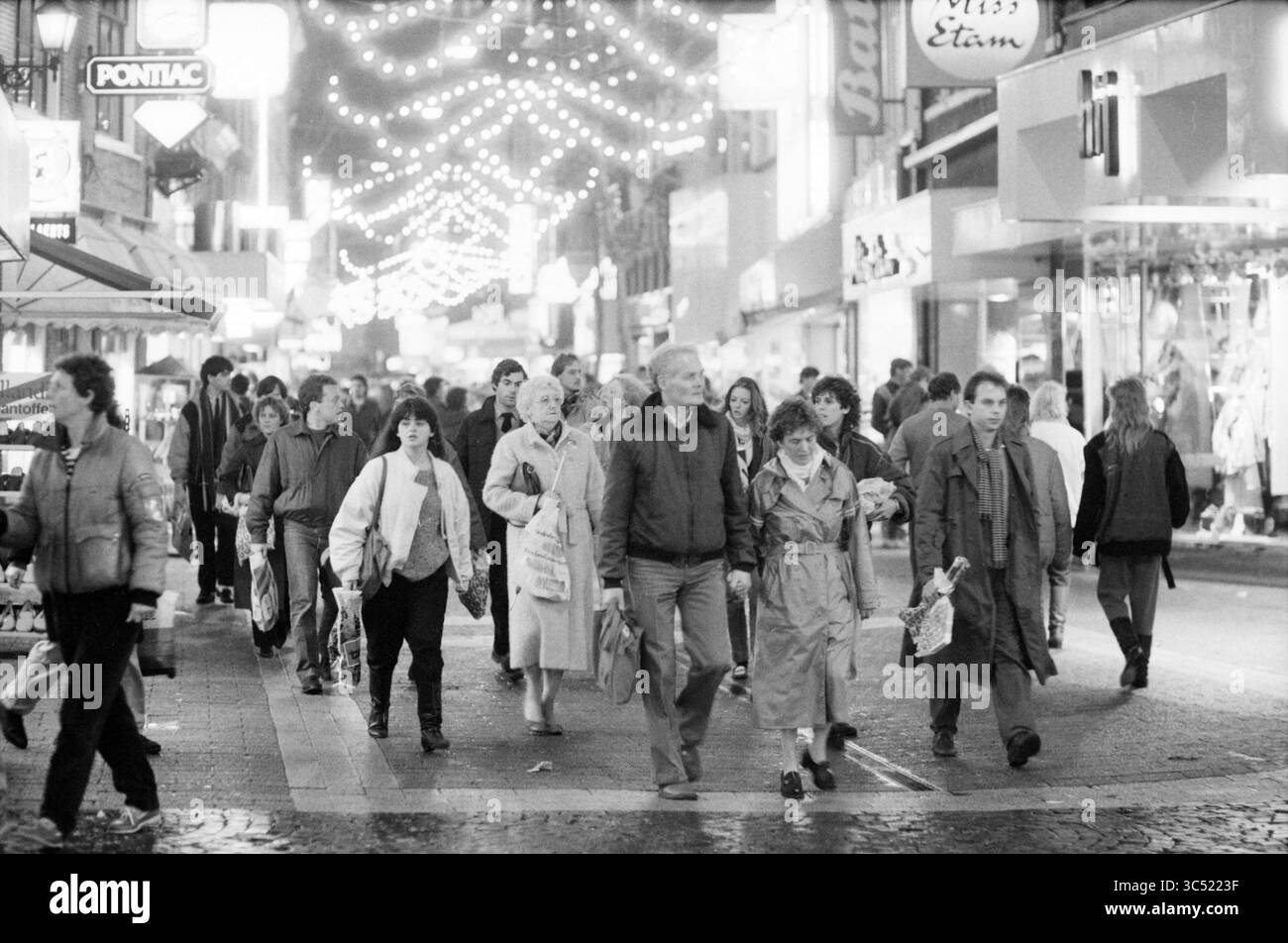 Einkaufsmöglichkeiten im Stadtzentrum von St. Nicolaas, Geschäfte und Kioske, 04.12-1985 Whizgle News, Dutch Desk, Niederlande, 1950-2000 Eine geschäftige Straßenszene voller Menschen, die unter festlichen Lichtern spazieren gehen, umgeben von Geschäften und Geschäften. Jeder trägt warme Kleidung, trägt Taschen und führt Gespräche, während er die lebhafte Atmosphäre genießt. Stockfoto