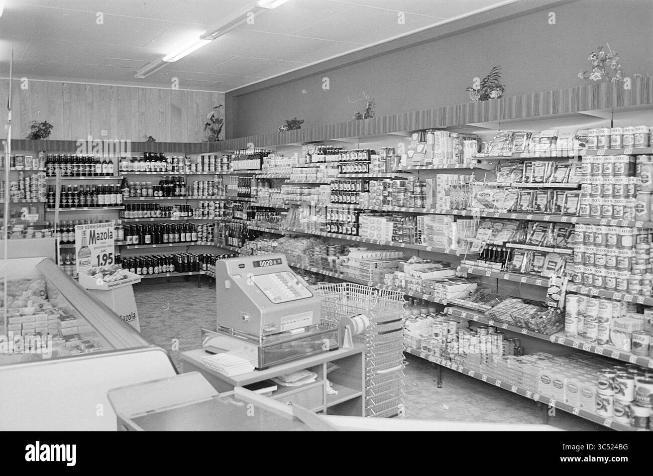 Innenraum Fa. Hoeben Heemskerk, Interior, 24-04-1967 Whizgle News, Dutch Desk, Niederlande, 1950-2000 Ein gut organisiertes Lebensmittelgeschäft mit übersichtlichen Regalen mit einer Vielzahl von Dosenwaren, Getränken und verpackten Produkten. Im Vordergrund ist ein Checkout-Bereich mit einer Kasse und einer Anzeige kleinerer Artikel zu sehen. Pflanzen schmücken die Regale und verleihen der Einkaufsumgebung einen Hauch von Grün. Stockfoto