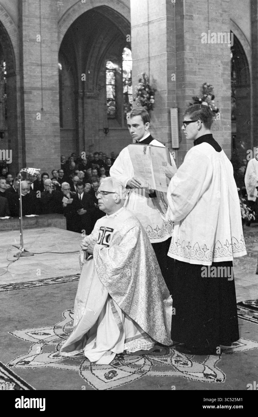 Eucharistiefeier. Whizgle News, Dutch Desk, Niederlande, 1950-2000 Eine feierliche religiöse Zeremonie findet in einer großen Kirche statt, in der ein sitzender Geistlicher in zeremonieller Kleidung sitzt. Zwei Assistenten stehen in der Nähe, einer hält ein Buch und der andere ist aufmerksam auf das Verfahren. Eine Gemeinde schaut leise im Hintergrund zu, was zur Atmosphäre der Ehrfurcht beiträgt. Stockfoto