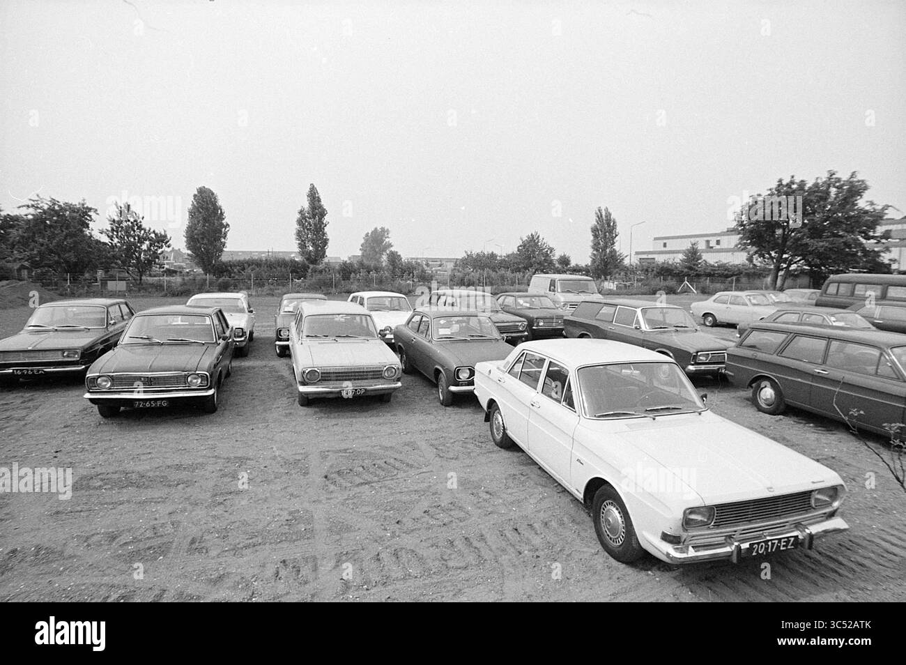 Parkplatz Whizgle News, Dutch Desk, Niederlande, 1950-2000 Eine Vielzahl von Autos, die auf einem offenen Gelände geparkt werden, mit klassischen Modellen und unterschiedlichen Stilen, umgeben von kargen Bäumen und offenen Flächen. Stockfoto