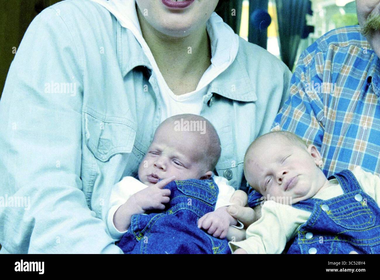Gemini Van Kooten, Haarlem, Niederlande, 21.03.2000 Whizgle News, Dutch Desk, Niederlande, 1950-2000 Ein lächelnder Junge wiegt zwei Neugeborene in passenden Denim-Overalls, wobei ein Baby spielerisch am Outfit des anderen zieht. Die Szene strahlt Wärme und Zärtlichkeit aus und fängt einen Moment der Freude und der Verbindung zwischen der Familie ein. Stockfoto