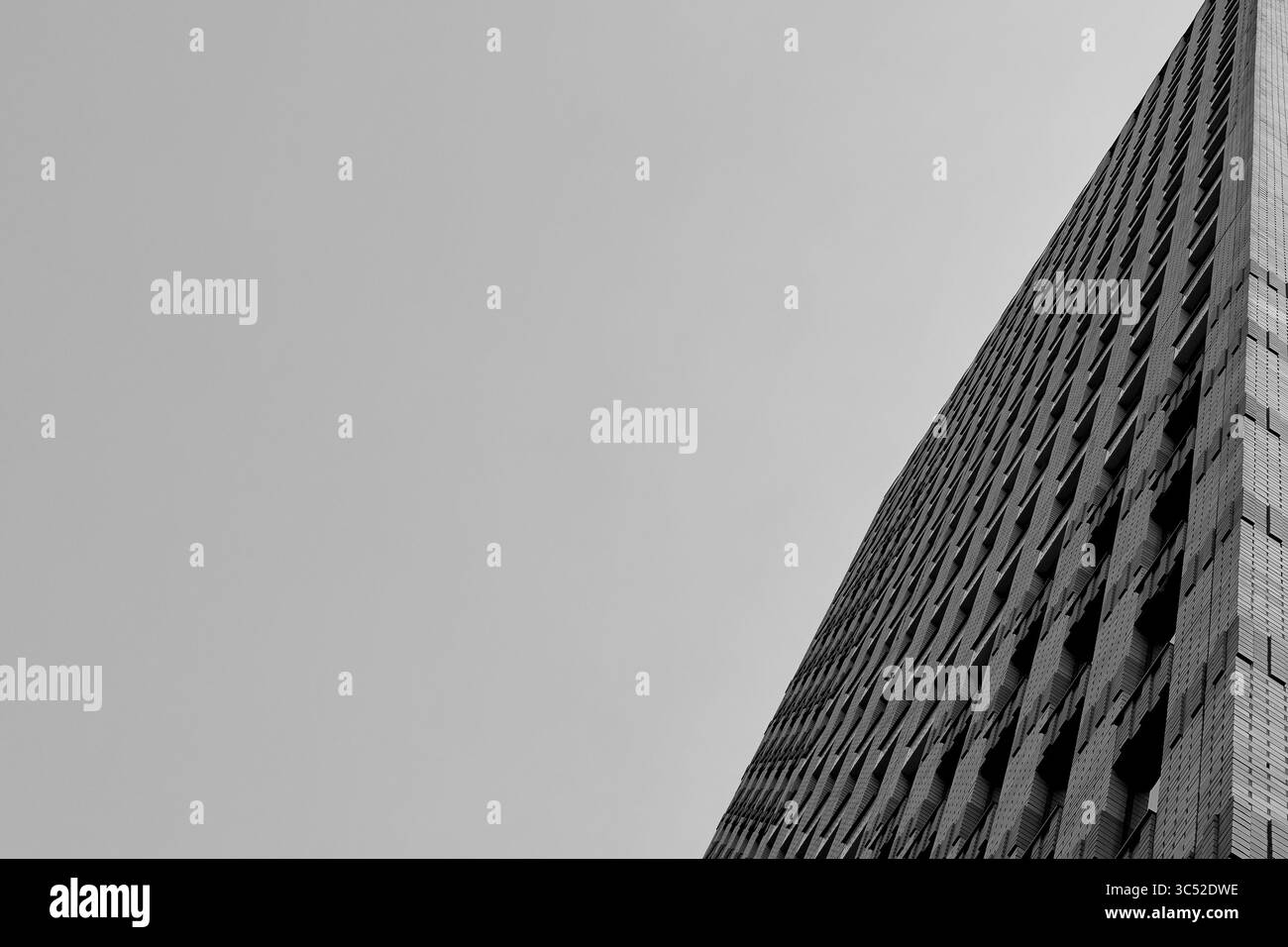 Der monochrome Blick auf den Turm des Symphony Hotels in Amsterdam setzt die gemusterten Fenster mit hellem Himmel in Kontrast und erzeugt ein beeindruckendes Gefühl von Höhe und Geometrie. Stockfoto