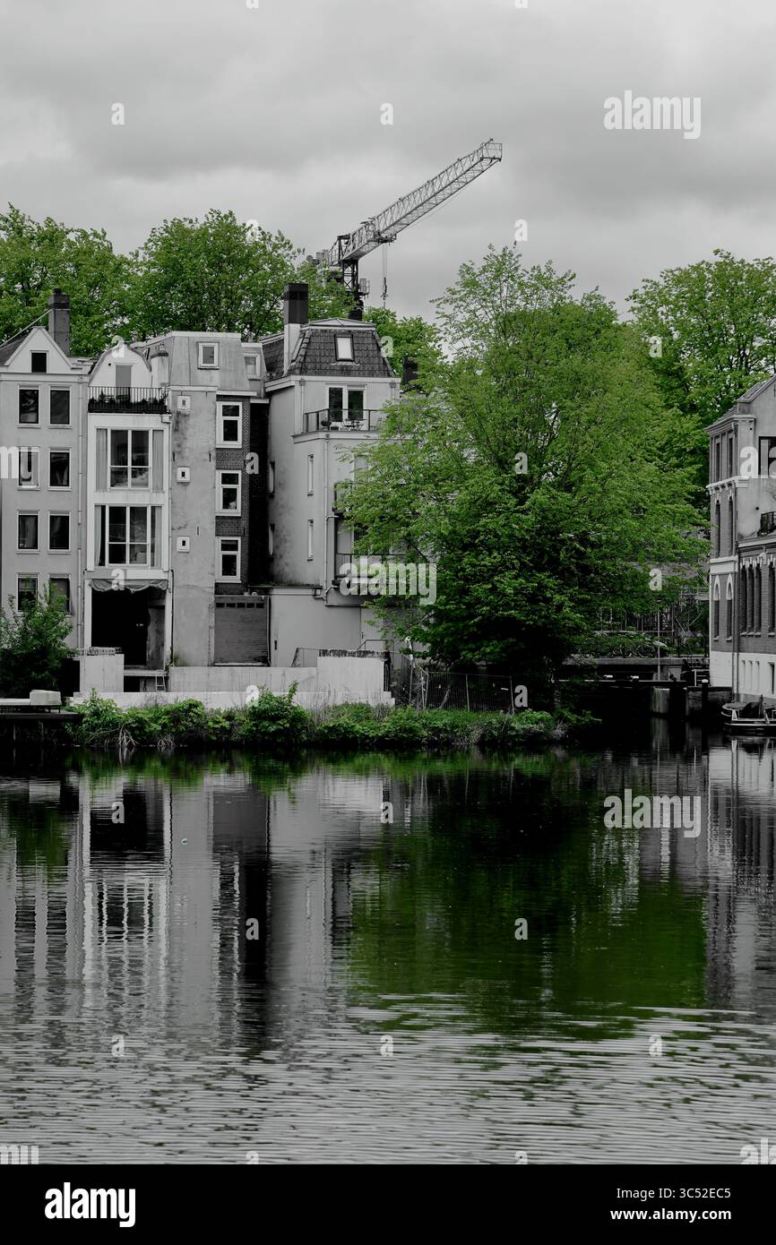 Der Blick von der Brücke Ezelsbrug in Amsterdam zeigt Kanalhäuser und einen Kran, der sich in ruhigem Wasser unter einem stimmungsvollen Himmel spiegelt. Stockfoto