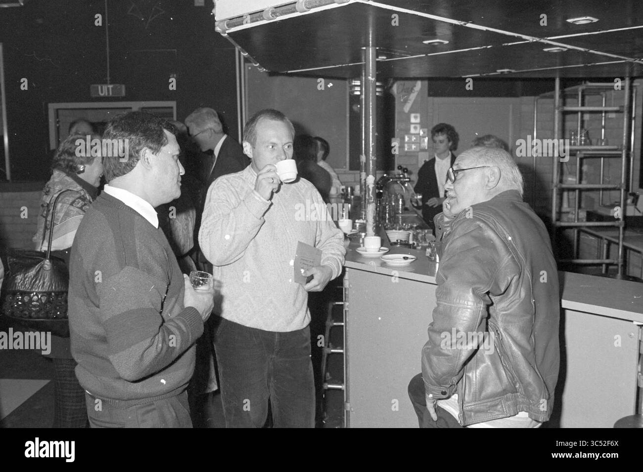 Abschied Kleywegt, Dwarsligger, 28.10.1991 Whizgle News, Dutch Desk, Niederlande, 1950-2000 Eine kleine Gruppe von Personen führt an einer Bar Gespräche, wobei eine Person aus einer Tasse schlürft, während eine andere einen Drink hält. Die Atmosphäre wirkt gesellig und entspannt, während sich andere im Hintergrund mischen. Stockfoto