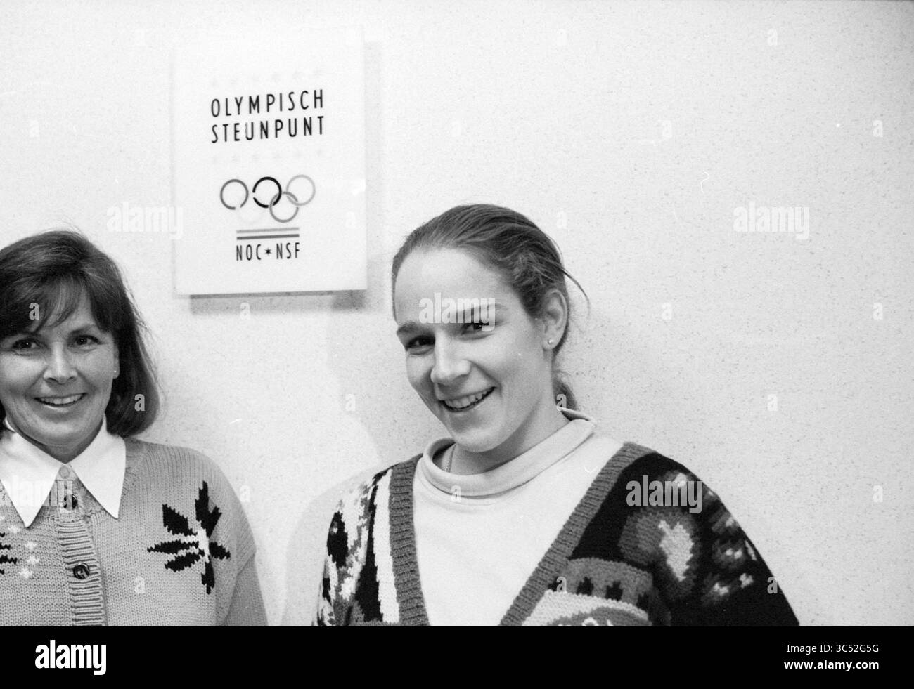 Kitty van Gilst + J. Gal, 20-12-1995 Whizgle News, Dutch Desk, Niederlande, 1950-2000 zwei Frauen stehen vor einem Schild mit der Aufschrift „Olympisch Steunpunt NOC*NSF“. Eine Frau mit langen Haaren lächelt hell, während sie einen gemusterten Pullover trägt, und die andere Frau mit kürzerem Haar steht mit freundlichem Ausdruck neben ihr. Stockfoto