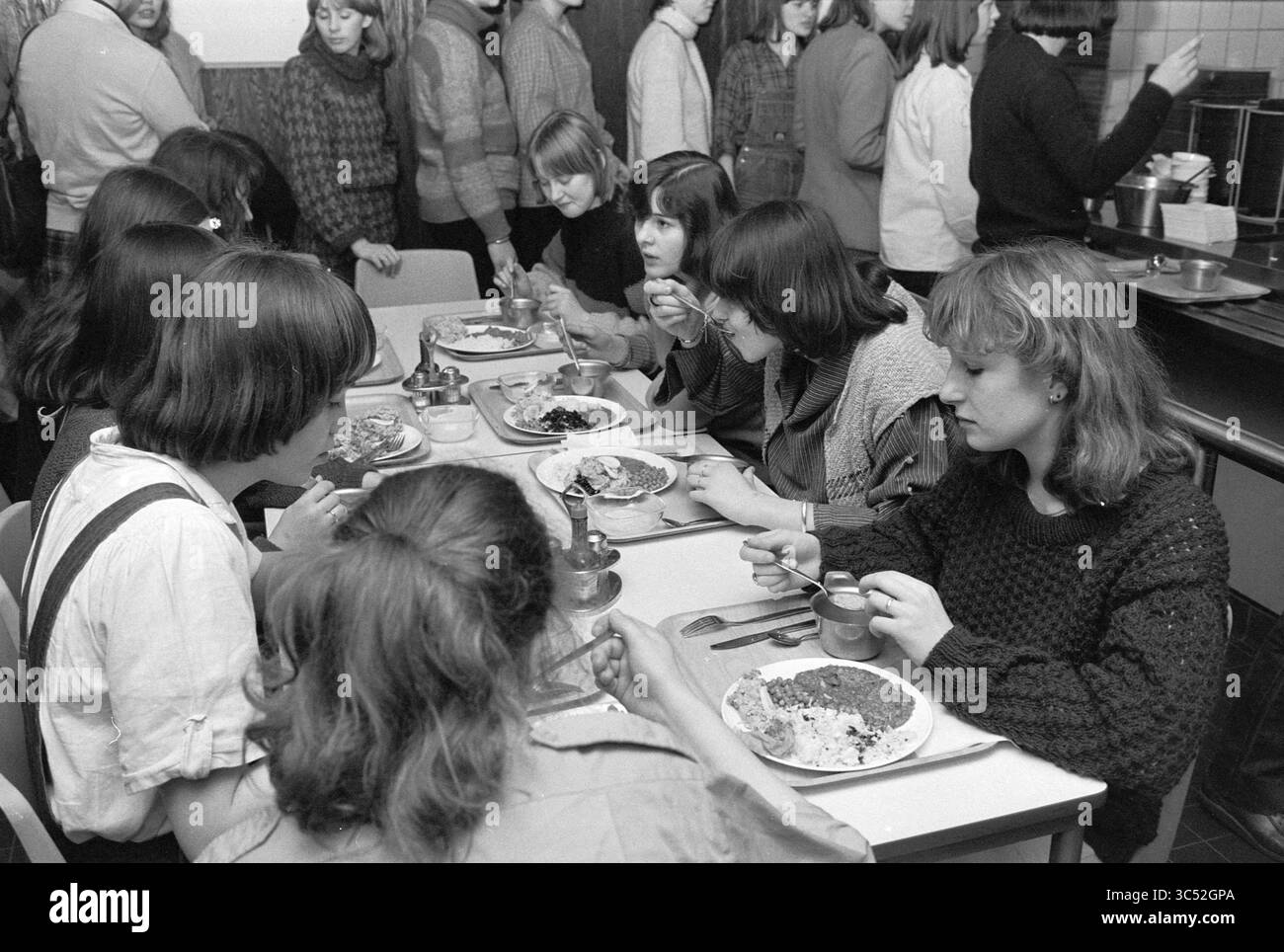 Jugendherberge, A'Dam, Jugendherbergen, Amsterdam, Niederlande, 01-03-1979 Whizgle News, Dutch Desk, Niederlande, 1950-2000 Eine Gruppe junger Frauen sitzt um einen Tisch, verbringt ein Mittagessen und schmeckt ihre Mahlzeiten. Sie lachen und unterhalten sich, während andere im Hintergrund stehen und eine lebhafte Atmosphäre schaffen. Die Szene fängt einen Moment der Kameradschaft und des gemeinsamen Erlebnisses ein. Stockfoto