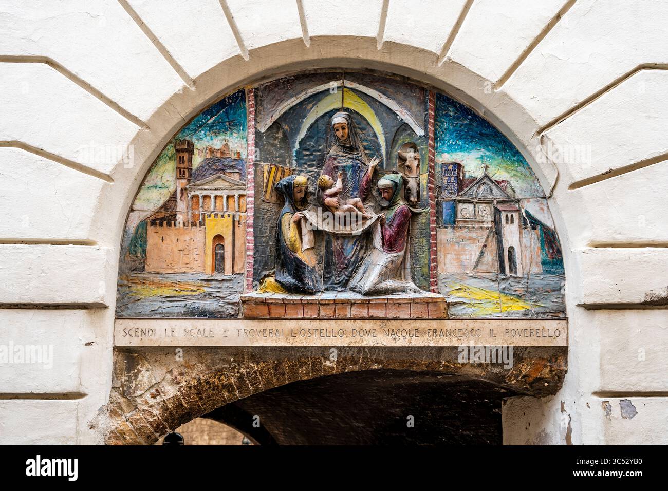 Dekorative Keramiklünette im Flachrelief mit der Darstellung des Heiligen Franziskus, der Jungfrau Maria und seiner Eltern in einer mittelalterlichen Straße von Assisi, Umbrien, Italien. Stockfoto