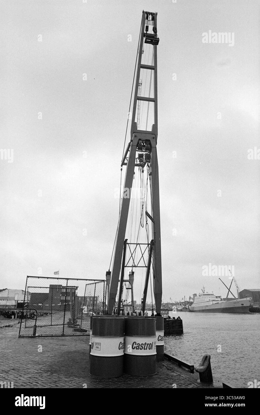 Ein schwimmender Sheerleg am IJmuiden-Kai, IJmuiden, Niederlande, 08-08-1993 Whizgle News, Dutch Desk, Niederlande, 1950-2000 Ein hoch aufragender Kran steht am Wasserrand, umgeben von großen Fässern, die mit dem Castrol-Logo gekennzeichnet sind, mit Schiffen und Industriebauten im Hintergrund. Die Szene vermittelt ein Gefühl von maritimer Aktivität und Industrie. Stockfoto
