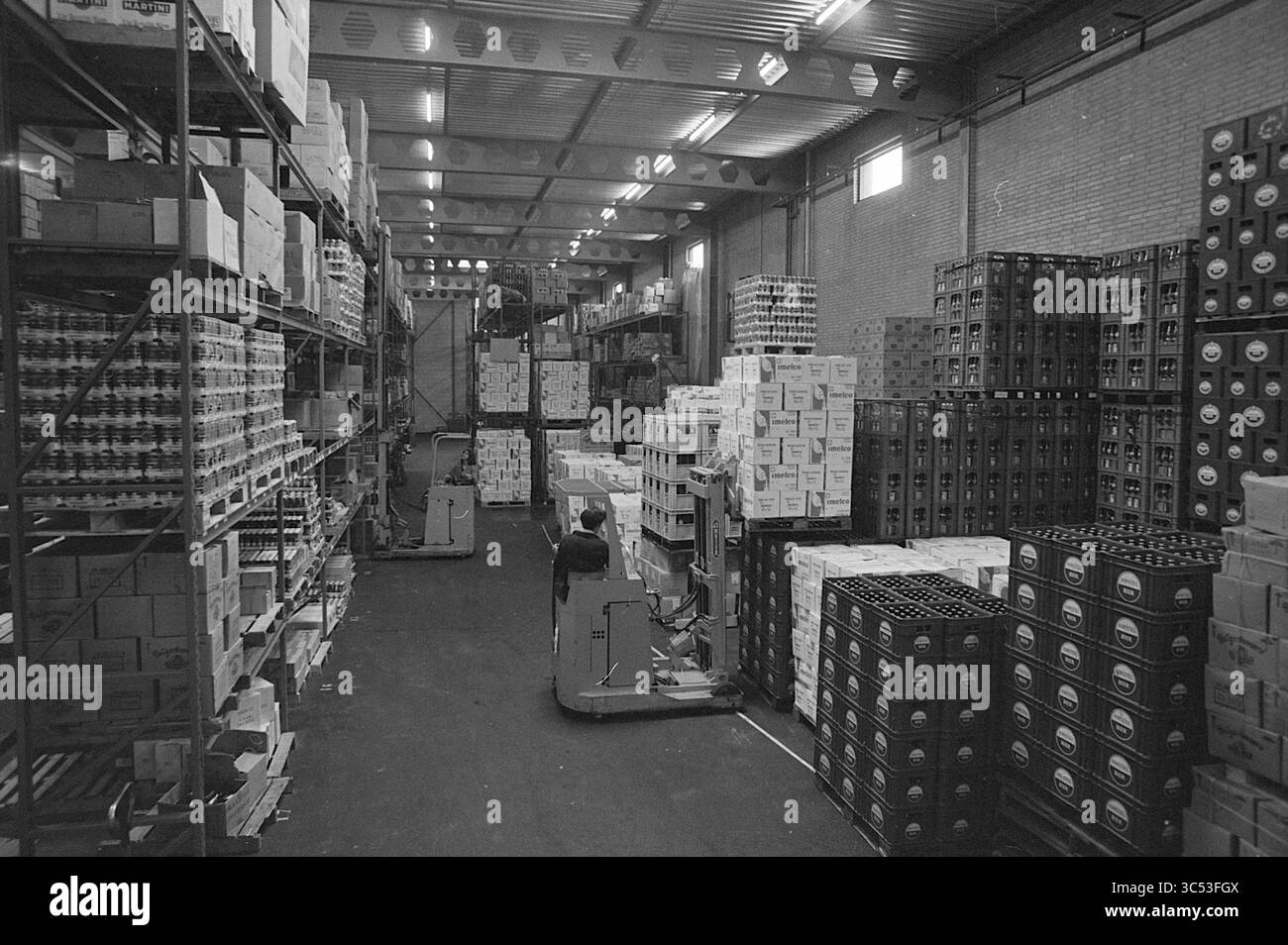 Warehouse Kijkgrip Beverwijk, Beverwijk, Niederlande, 01-05-1973 Whizgle News, Dutch Desk, Niederlande, 1950-2000 Ein geräumiges Lager mit ordentlich organisierten Regalen, hoch gestapelt mit Kisten und Kisten. Im Vordergrund fährt ein Arbeiter einen Gabelstapler zwischen den Gängen, umgeben von einer Vielzahl von verpackten Waren. Die Atmosphäre ist voll und doch geordnet, was ein gut verwaltetes Inventar widerspiegelt. Stockfoto