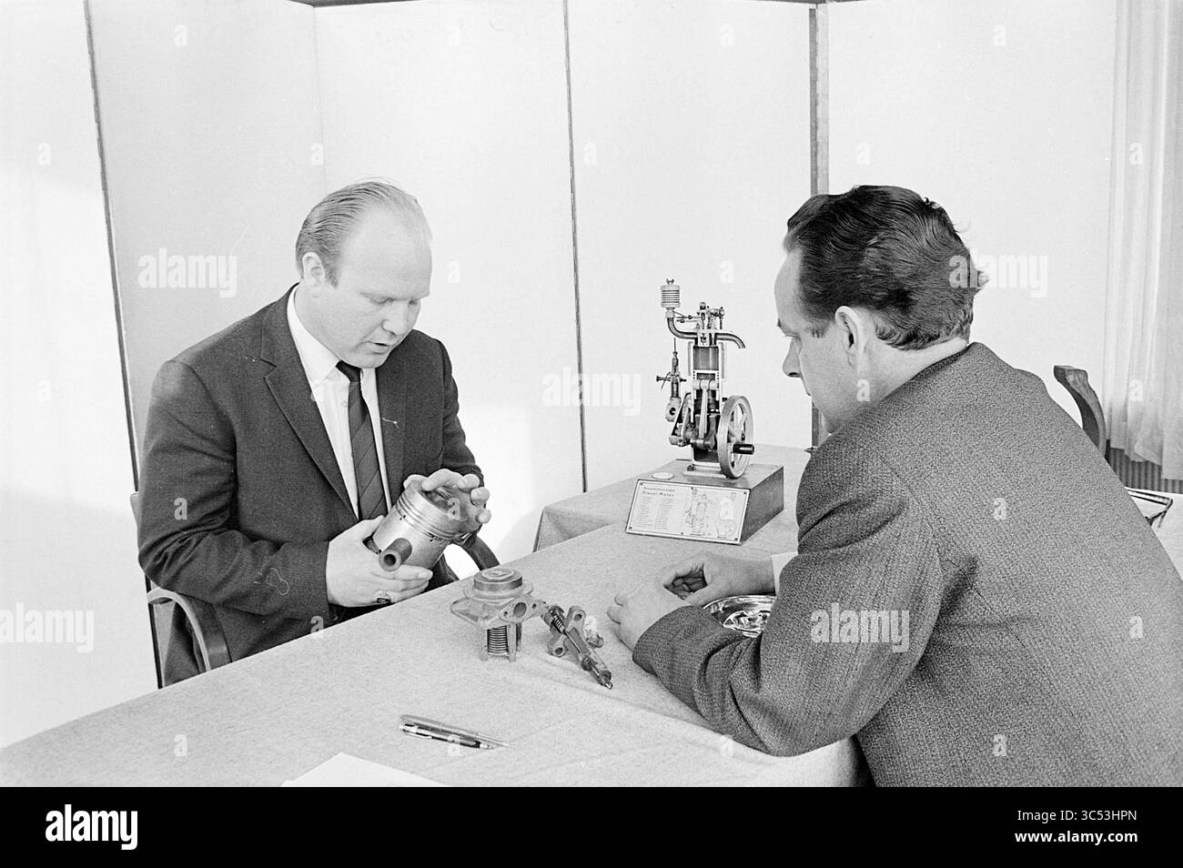 Fahrerprüfung NZH, Noord Zuid Hollandse Vervoersmaatschappij N.V., NZ, 22-04-1969 Whizgle News, Dutch Desk, Niederlande, 1950-2000 zwei Männer diskutieren an einem Tisch, der mit verschiedenen mechanischen Teilen und Bauteilen besprochen wird, ausführlich. Ein Mann untersucht ein kleines Motorbauteil in der Hand, während der andere aufmerksam beobachtet und einen technischen oder technischen Schwerpunkt in seinem Gespräch vorschlägt. In der Tabelle wird auch ein Motormodell angezeigt, das eine mögliche Demonstration oder Analyse der mechanischen Konstruktion angibt. Stockfoto