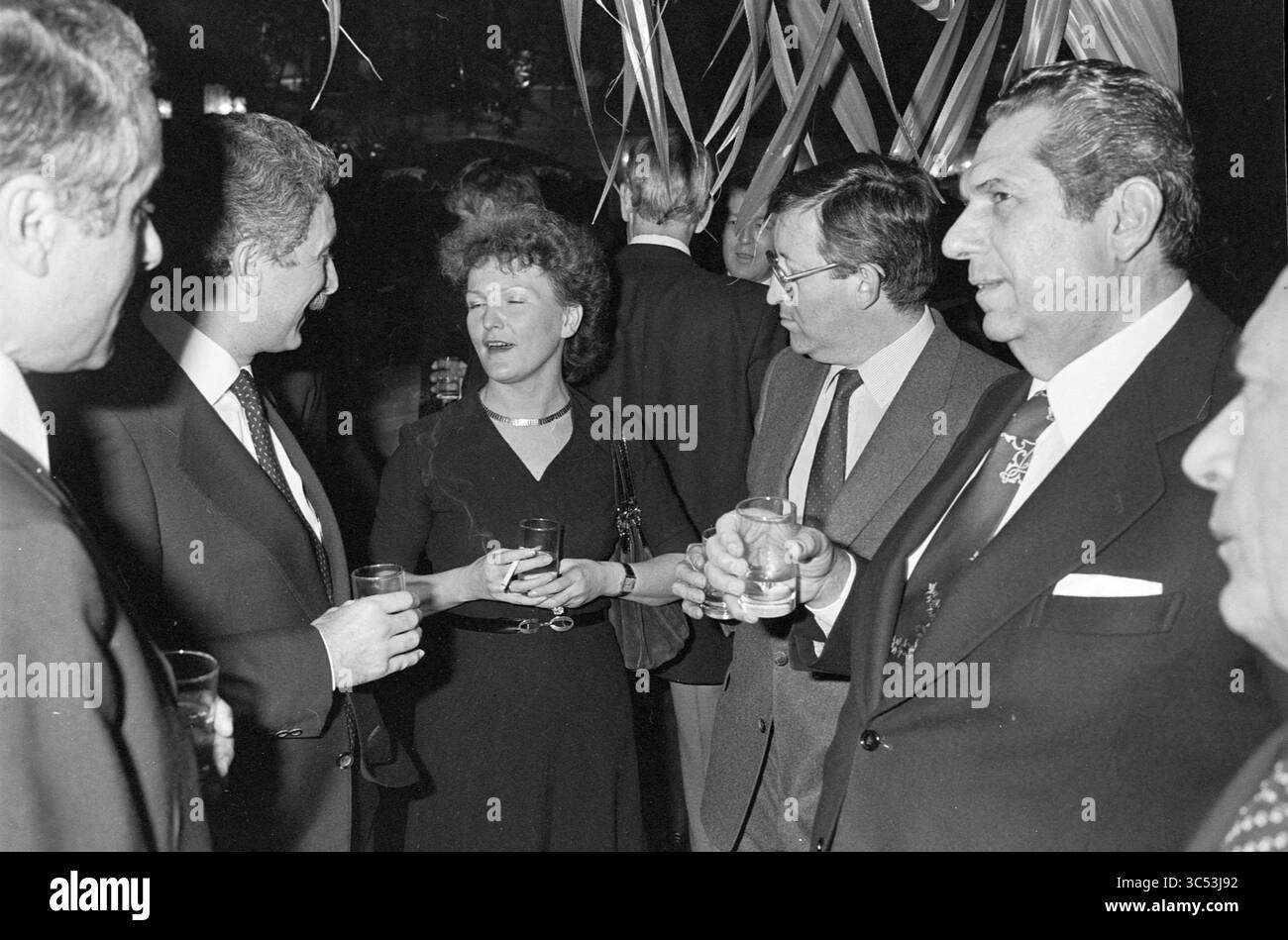 Einige Gentlemen bei einem Empfang Whizgle News, Dutch Desk, Niederlande, 1950-2000 Eine Gruppe elegant gekleideter Personen führt bei einem geselligen Treffen Gespräche, mit einer Mischung aus Lachen und Intrigen, während sie Drinks genießen. Die Atmosphäre spiegelt eine Mischung aus Raffinesse und Kameradschaft vor festlicher Kulisse wider. Stockfoto