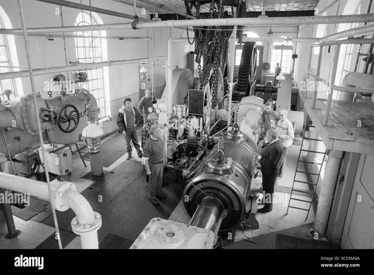 Wiedereröffnung der Dampfpumpenstation auf halbem Wege, Eröffnung, Öffnungen, Inbetriebnahme, Dampfpumpenstation und Dampfpumpenstation, Halfweg, 01-04-1989 Whizgle News, Dutch Desk, Niederlande, 1950-2000 Eine Gruppe von Ingenieuren und Technikern arbeitet in einer großen Industrieanlage zusammen, die von komplexen Maschinen und Rohren umgeben ist. Der Raum ist mit verschiedenen Anlagen gefüllt, darunter eine prominente Turbine oder ein Generator in der Mitte, was die Komplexität der laufenden Vorgänge unterstreicht. Die Atmosphäre deutet auf eine Zusammenarbeit in einem technischen Umfeld hin. Stockfoto