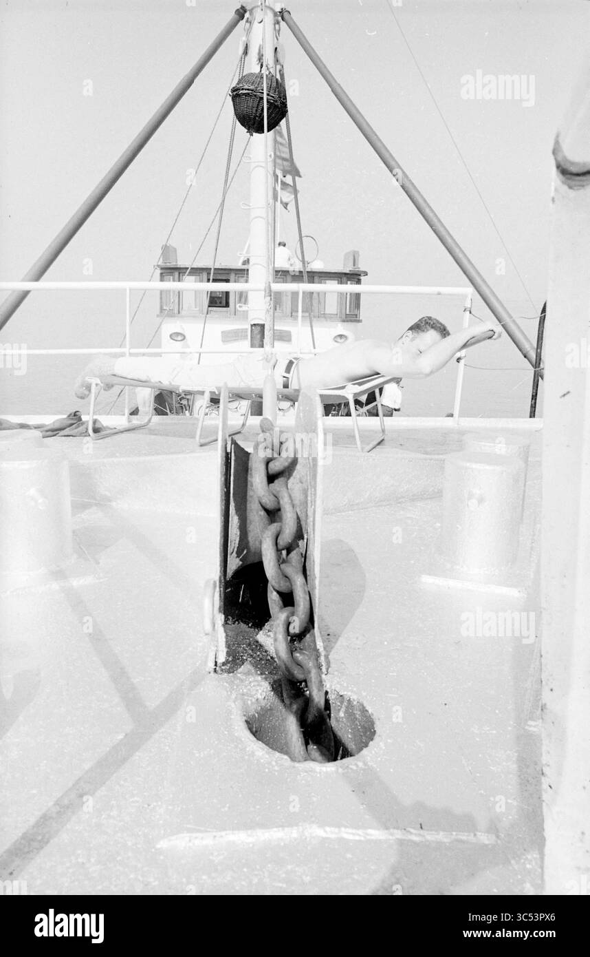 Report Sea Fishing., Angling, 14-05-1965 Whizgle News, Dutch Desk, Niederlande, 1950-2000 eine Ankerkette führt durch ein Loch im Deck hinunter zum Ozean, wobei im Hintergrund ein Schiffsmast und eine Kabine sichtbar sind. Die Szene fängt einen Moment auf einem Schiff ein und betont die Verbindung zwischen Schiff und Meer. Stockfoto