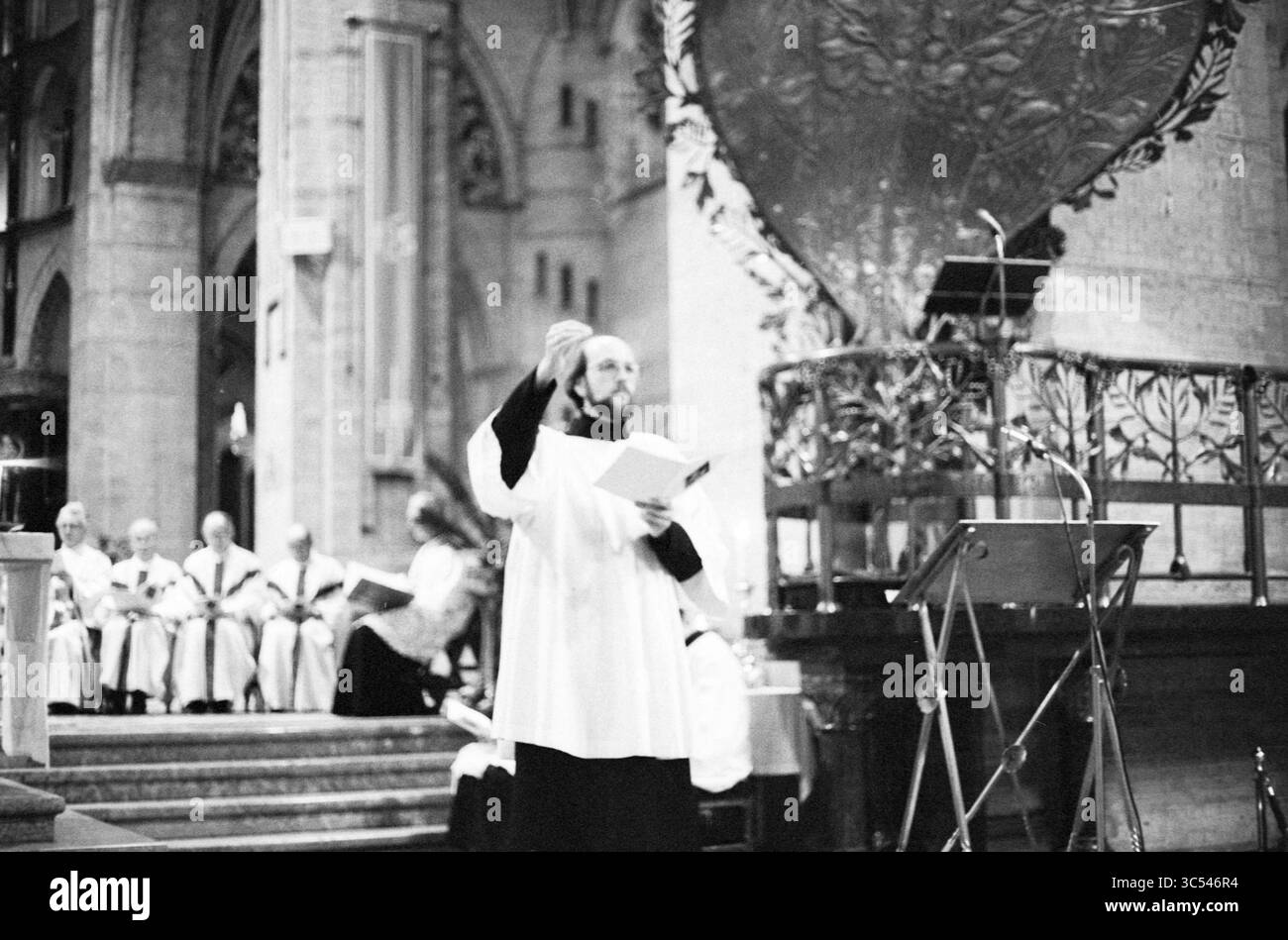 Heilige Öl-Basilika Haarlem, Kirchen, 04-04-1980 Whizgle News, Dutch Desk, Niederlande, 1950-2000 Ein Geistlicher steht in einer prominenten Pose, hält ein Buch und gibt während eines zeremoniellen Ereignisses Gesten, während eine Gruppe von Geistlichen-Kollegen im Hintergrund sitzt, alles in der Pracht eines kunstvollen Innenraums. Stockfoto