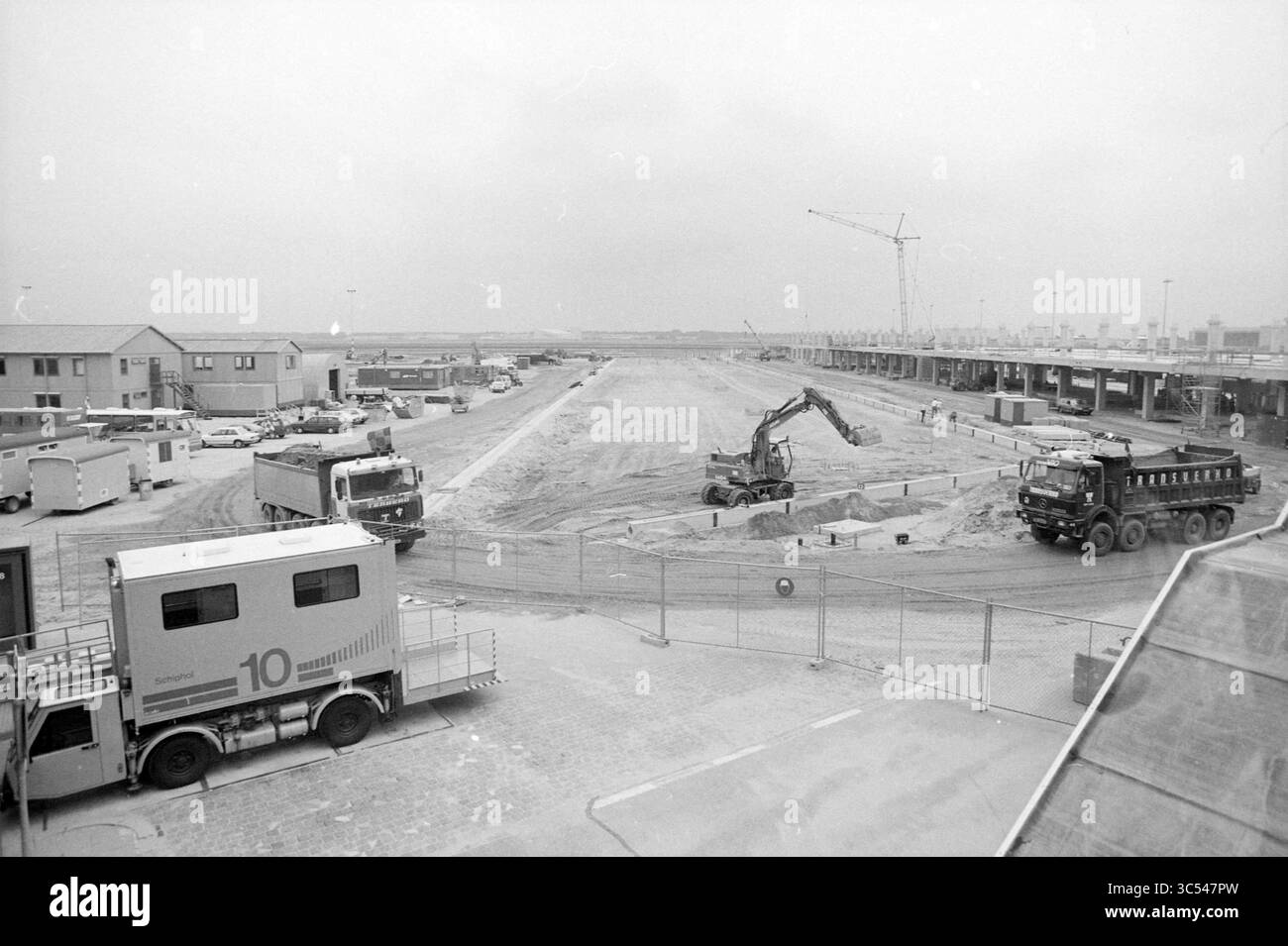 Work B-Pier Schiphol, Schiphol, 21.08.1989 Whizgle News, Dutch Desk, Niederlande, 1950-2000 Eine Baustelle mit schweren Maschinen, einschließlich Bagger und Muldenkipper, sowie verschiedenen Fahrzeugen und provisorischen Bauwerken. Das Gebiet scheint in erheblichem Maße ausgebaut oder erweitert zu werden, wobei im Hintergrund Krane sichtbar sind und ein umzäunter Umkreis Sicherheitsmaßnahmen anzeigt. Stockfoto