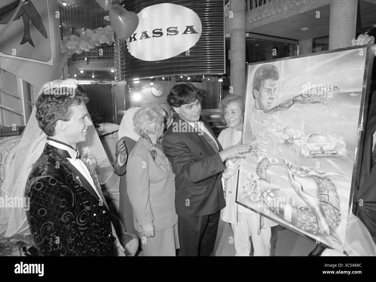 Empfang Jan Lammers, Z'voort, Zandvoort, 13-02-1992 Whizgle News, Dutch Desk, Niederlande, 1950-2000 Eine Gruppe elegant gekleideter Individuen versammelt sich in einem feierlichen Rahmen, wobei eine Person ein großes, lebendiges Gemälde mit zwei Gesichtern und symbolischen Elementen präsentiert. Die Atmosphäre ist festlich und bietet eine Mischung aus Spannung und Bewunderung unter den Teilnehmern. Stockfoto