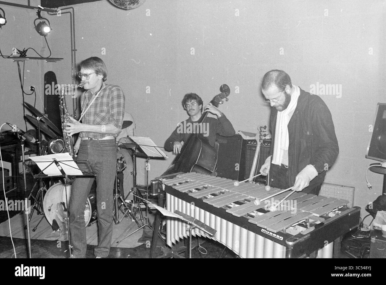 Musik-Performance, 00-01-1981 Whizgle News, Dutch Desk, Niederlande, 1950-2000 Ein Trio von Musikern tritt in einer intimen Umgebung auf und zeigt ihre Talente mit einem Saxophonisten, einem Bassisten und einem Vibraphonisten, die alle tief in den Moment verwickelt sind. Noten sind sichtbar und deuten auf die strukturierte, aber improvisierende Art ihrer Performance hin. Stockfoto