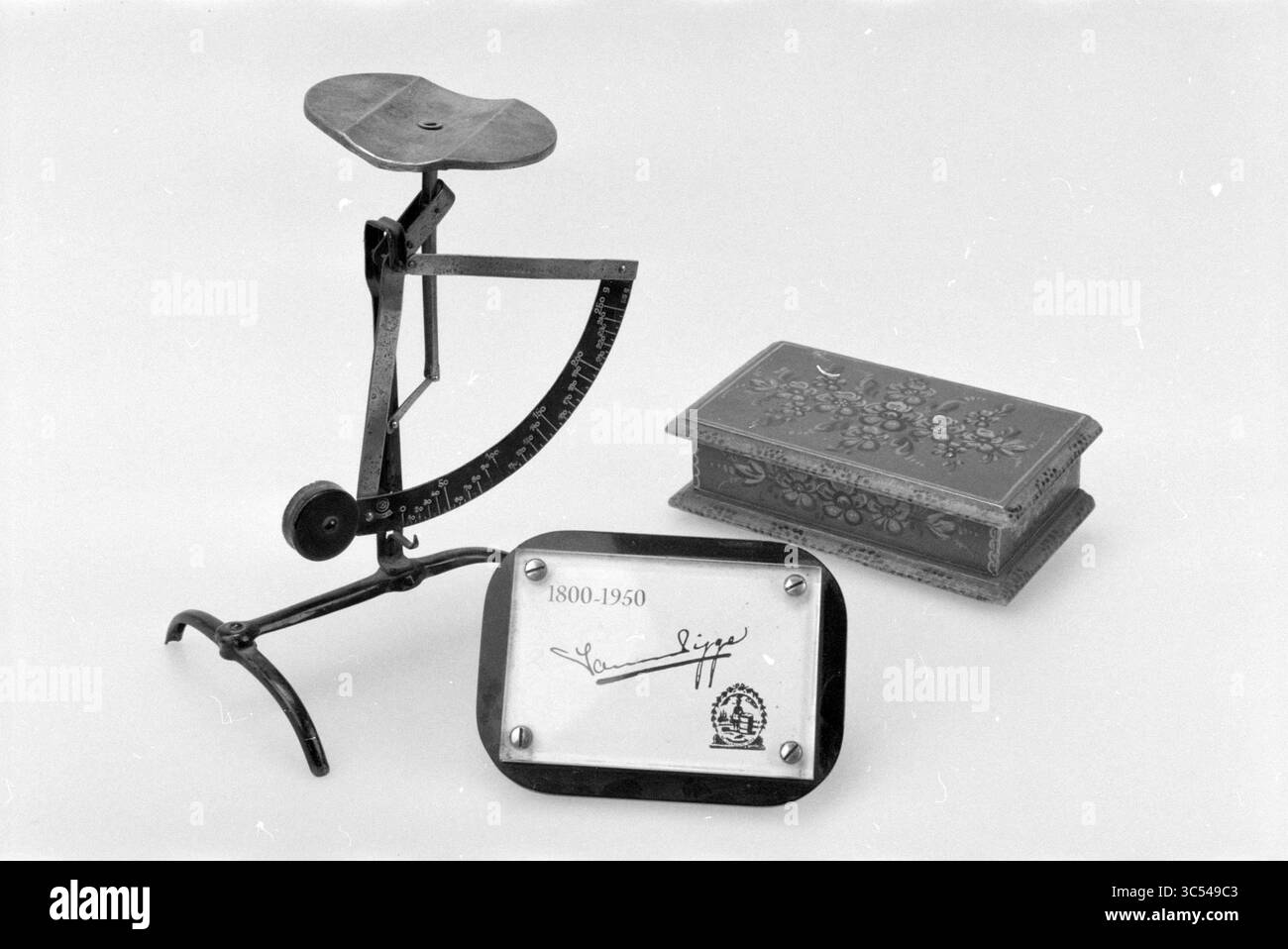 Verschiedene Artikel J. v.d. Pigge 200 Jahre, Haarlem, Niederlande, 23-02-2000 Whizgle News, Dutch Desk, Niederlande, 1950-2000 Eine Vintage-Waage, eine dekorative Holzkiste mit Blumenmotiven und eine von einem Künstler signierte Gedenktafel an die Jahre 1800-1950. Stockfoto