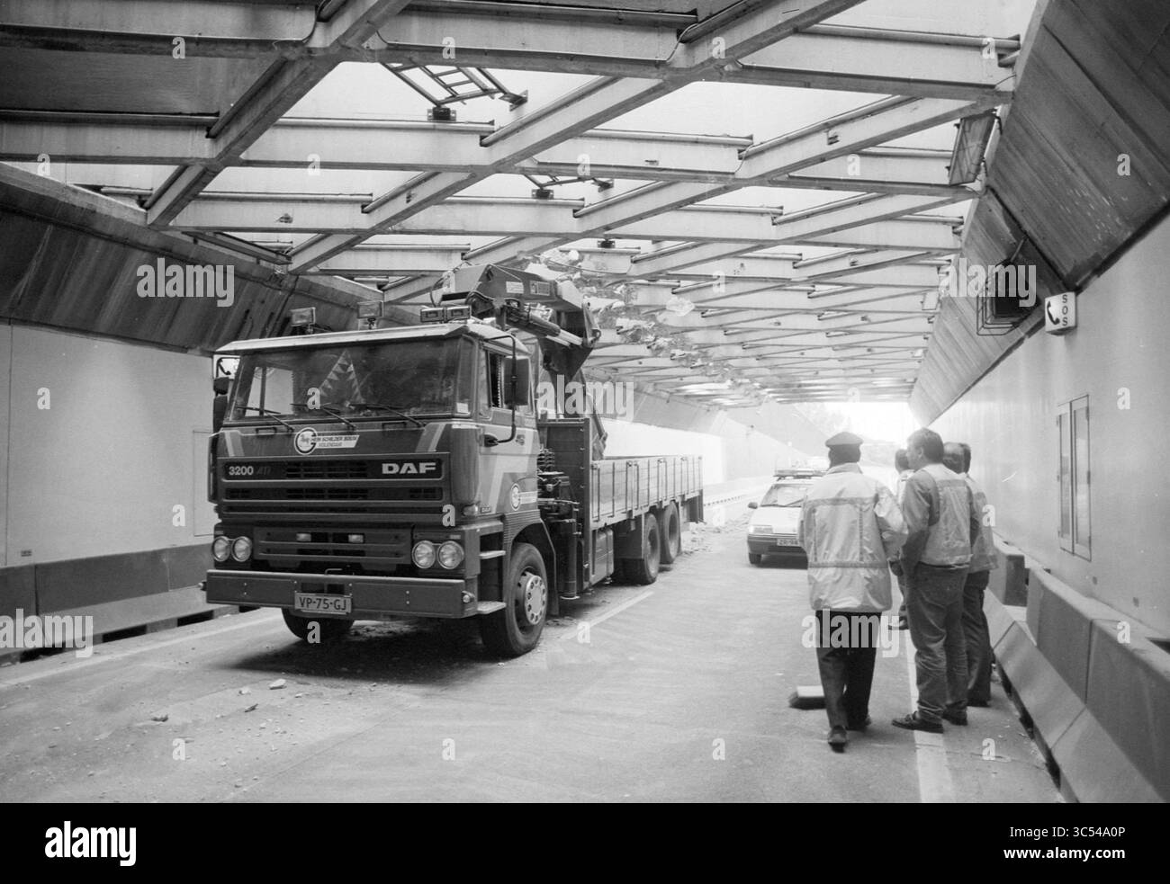 Unfall, Velsertunnel, 12-07-1993 Whizgle News, Dutch Desk, Niederlande, 1950-2000 Ein großer Lkw fährt durch einen Tunnel, dessen Abteil angehoben ist, während zwei Personen von der Seite aus beobachten. Die Szene ist geprägt von einem Gefühl von Aktivität und Struktur, die die einzigartige Umgebung des Tunnels zeigt. Stockfoto