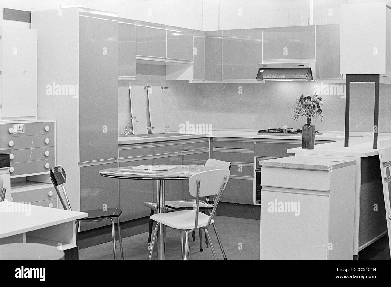 Intr. Bowl-Dauer auf dem Rijksstraatweg, Interior, Haarlem, Rijksstraatweg, Niederlande, 27-09-1974 Whizgle News, Dutch Desk, Niederlande, 1950-2000 Eine moderne Küche mit eleganten Schränken und stilvollem Layout, komplett mit einem runden Esstisch, umgeben von minimalistischen Stühlen. Eine kleine Blumenvase verleiht dem modernen Design einen Hauch Wärme. Stockfoto