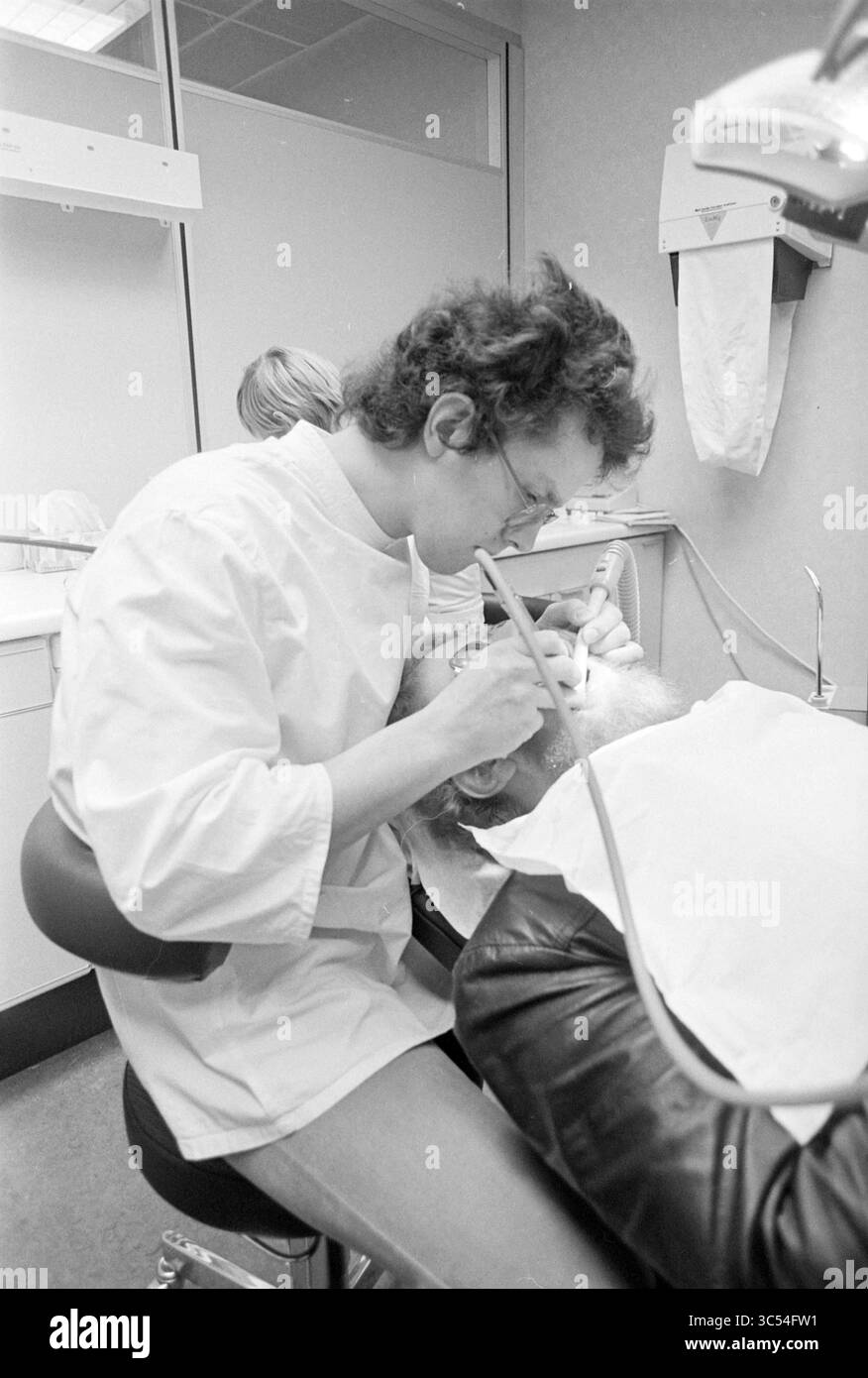 Zahnarzt Zonnenberg IJmuiden, Zähne, Zahnärzte, 04-02-1976 Whizgle News, Dutch Desk, Niederlande, 1950-2000 Ein Zahnarzt konzentriert sich auf den Mund eines Patienten, während er Zahngeräte verwendet, und zeigt einen Moment der sorgfältigen Aufmerksamkeit in einer klinischen Umgebung. Eine zweite Person ist im Hintergrund sichtbar, die den Vorgang möglicherweise unterstützt oder beobachtet. Stockfoto